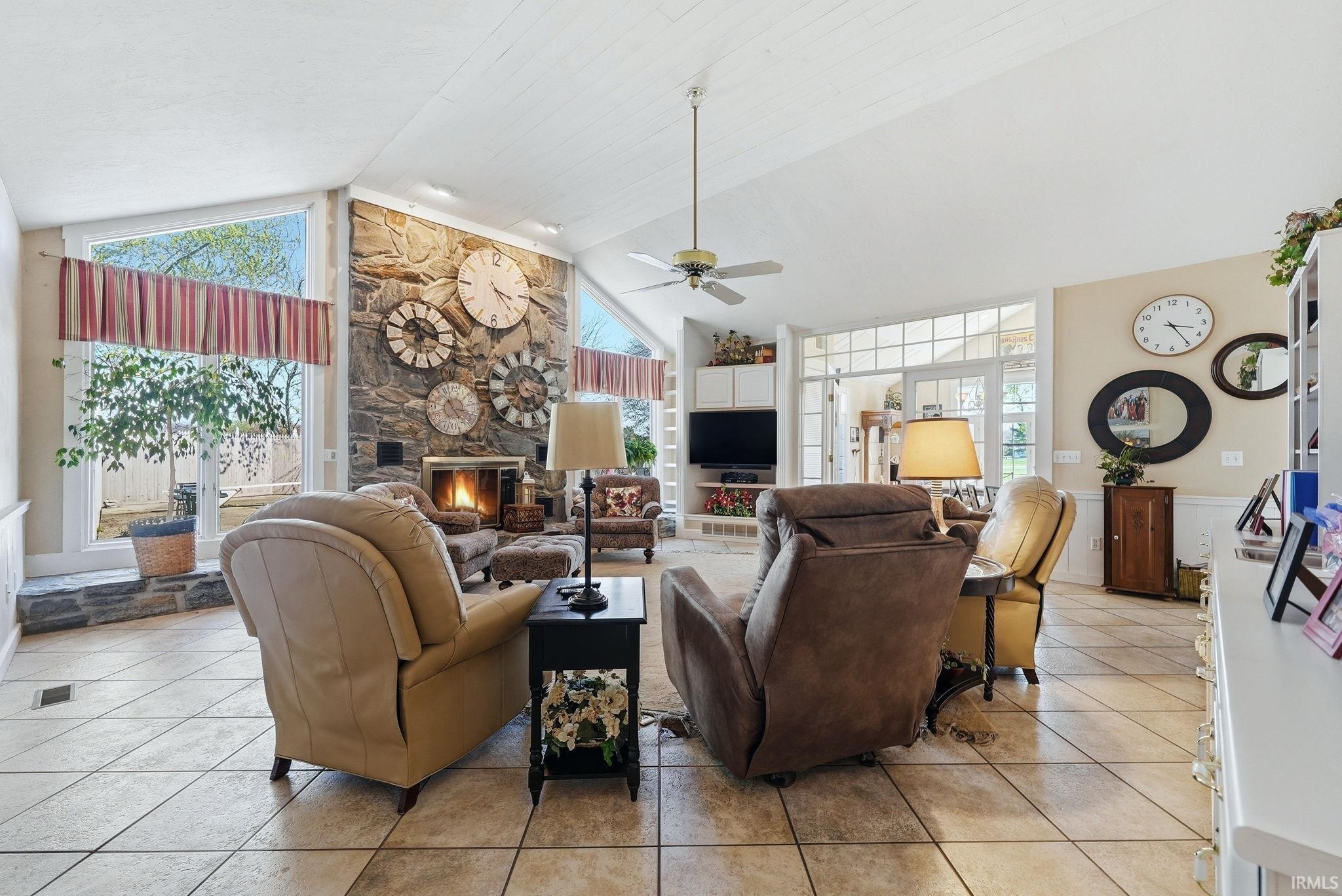 Living room with light tile patterned floors, a stone fireplace, ceiling fan, and a high ceiling