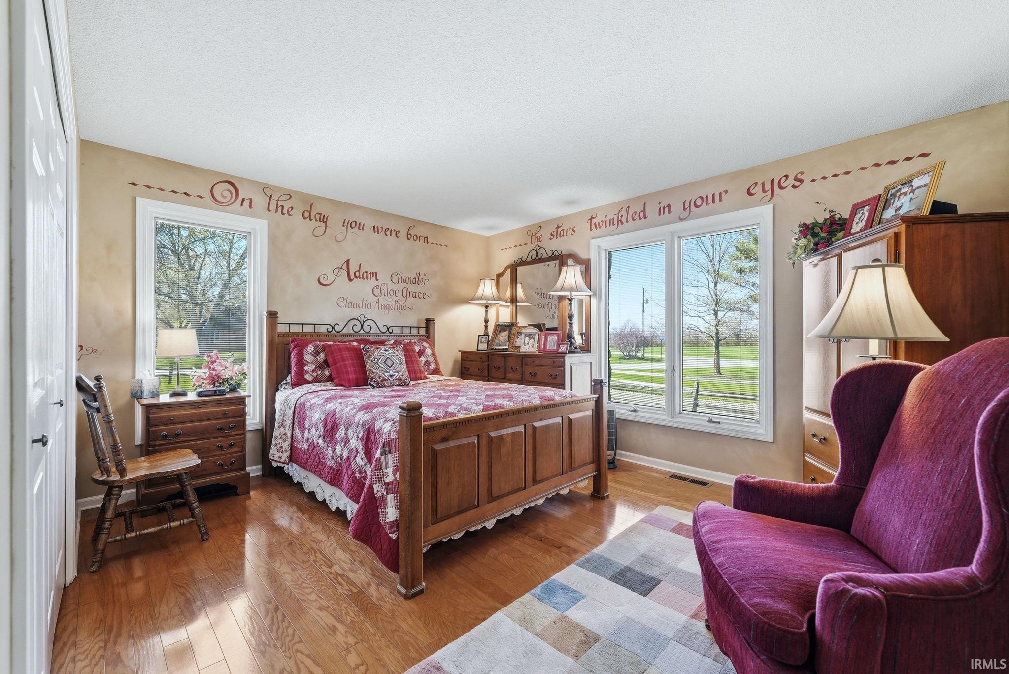 Bedroom with light wood-style floors, multiple windows, and a textured ceiling