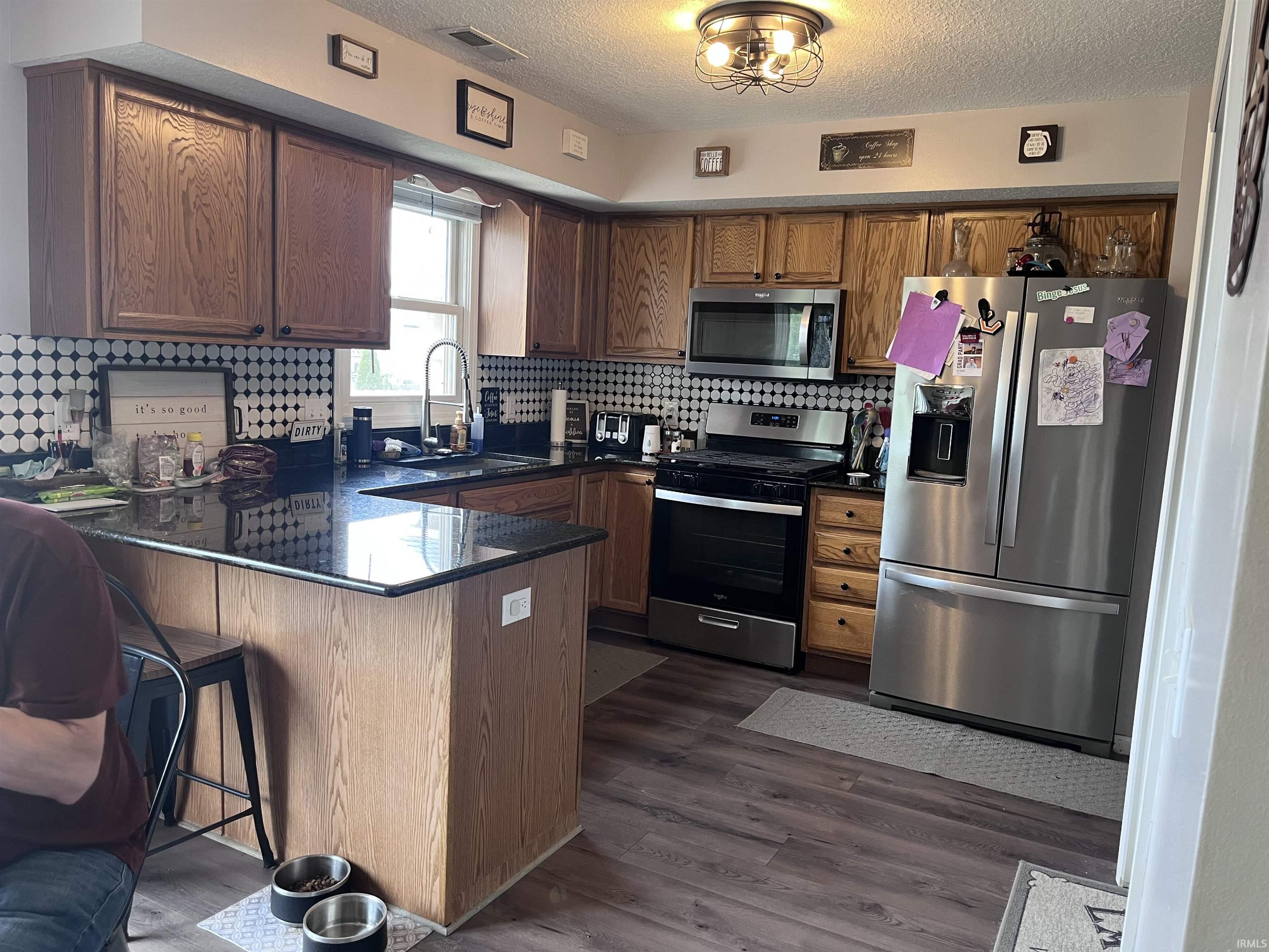 Kitchen featuring wood cabinetry, stainless steel appliances, dark countertops, and a mosaic tile backsplash