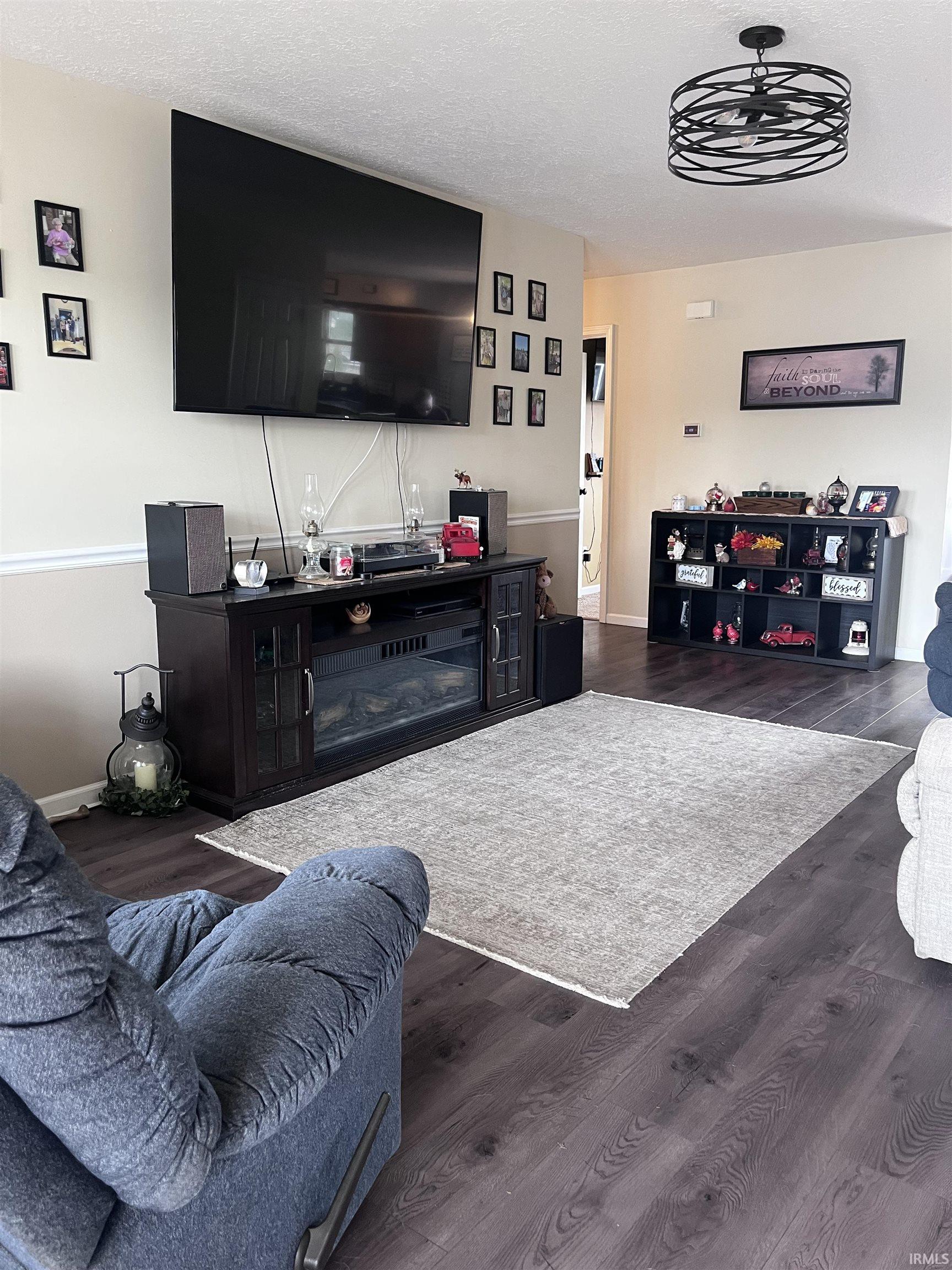 Spacious living area featuring wood-finish flooring, a contemporary ceiling fixture, and neutral wall tones with a chair rail accent