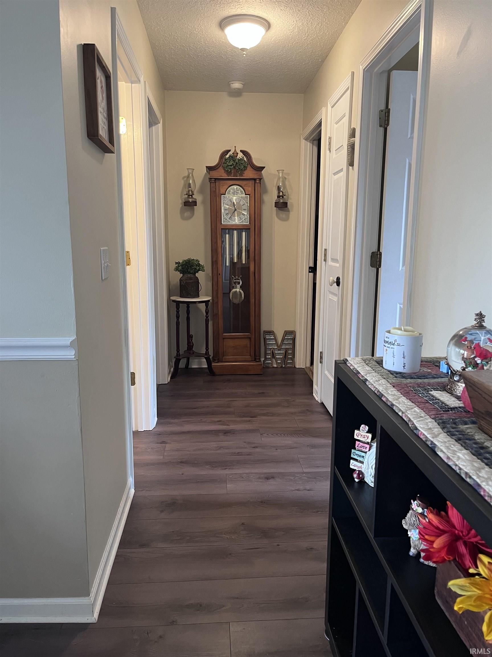 Hallway featuring dark wood-finish flooring, light tan walls with white trim, and recessed doorways