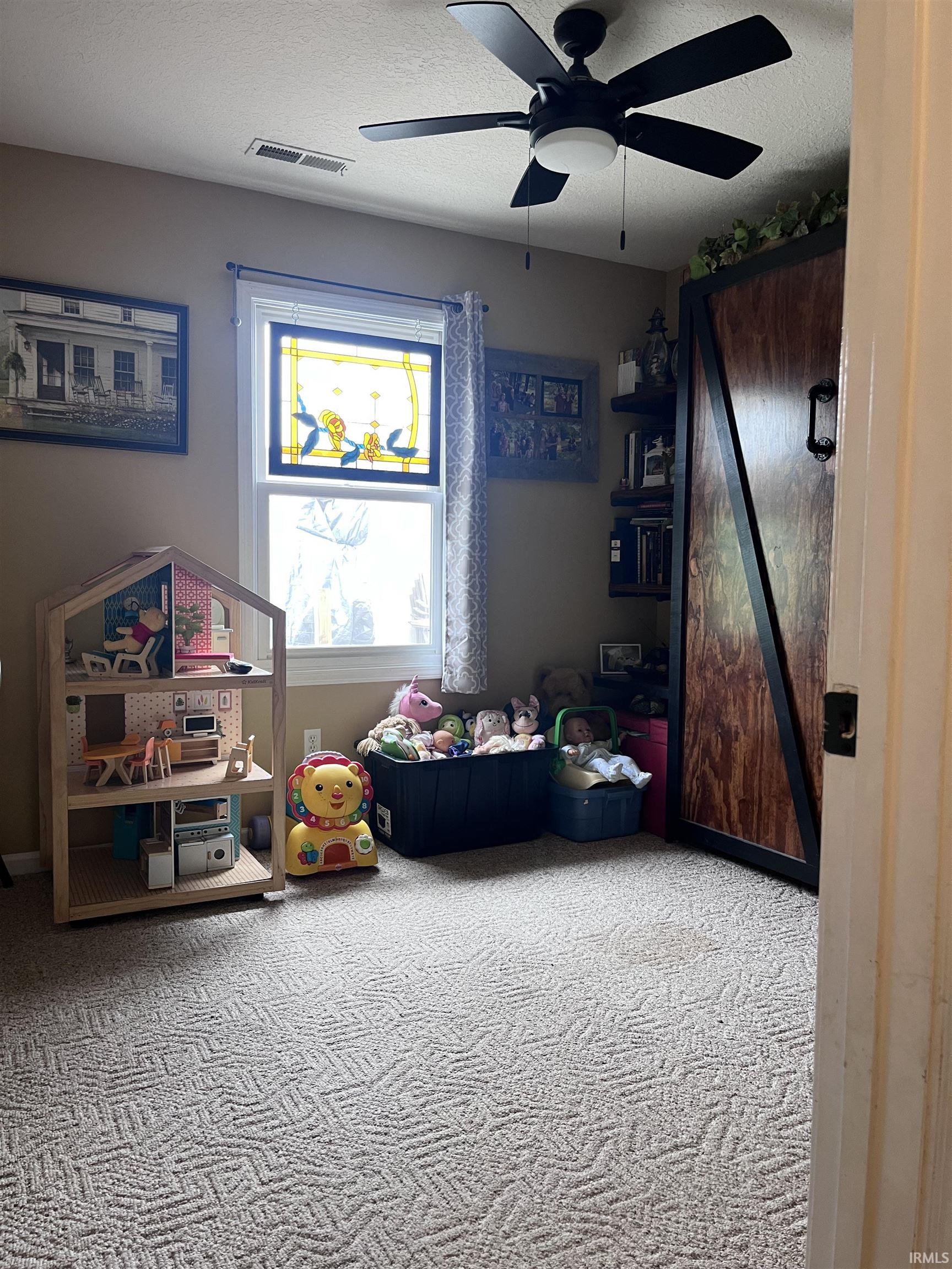 Wall-to-wall patterned carpeting, ceiling fan with integrated lighting, window with decorative stained glass, built-in shelving, and a wood-paneled sliding door