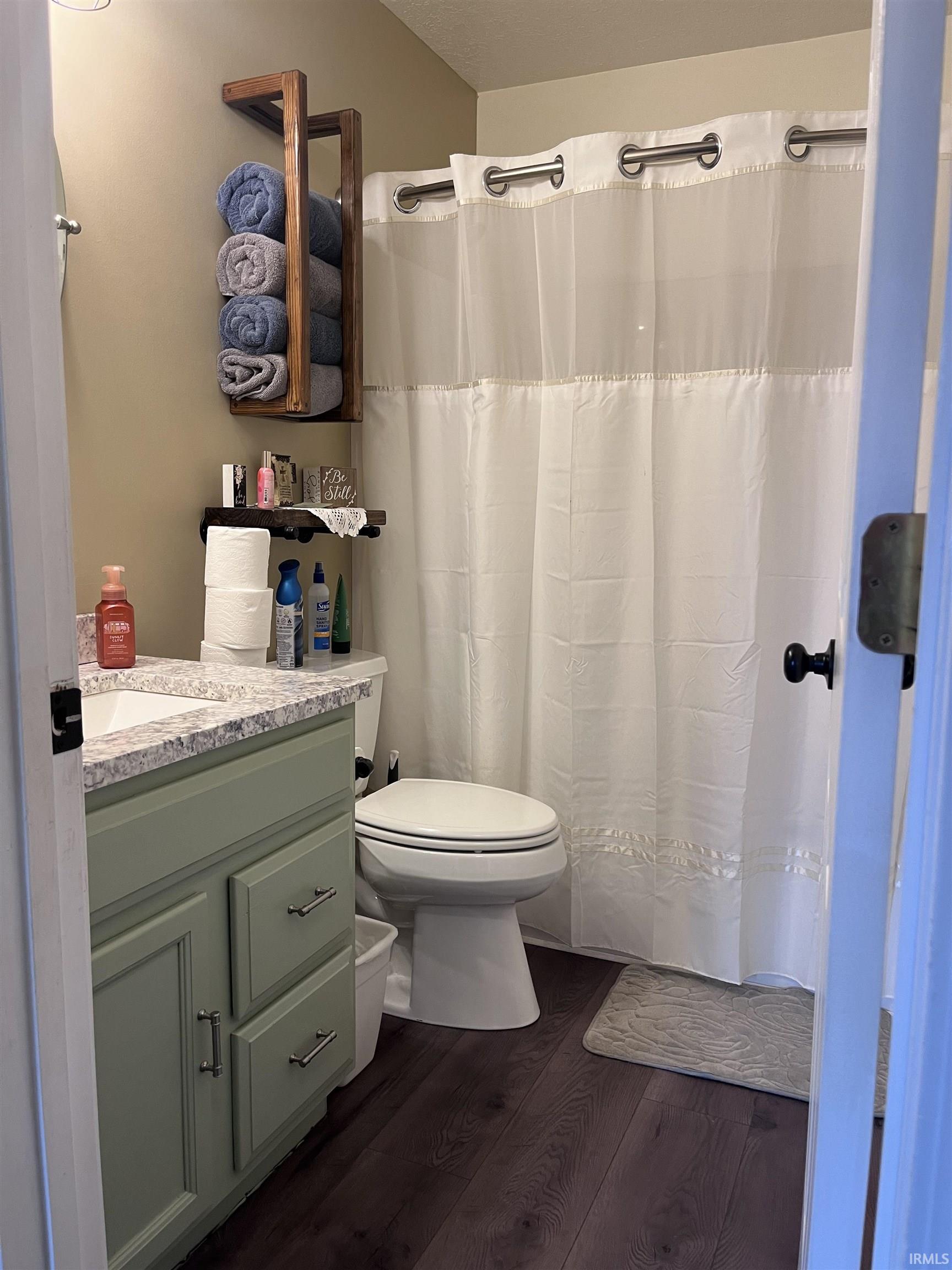 Bathroom featuring a sage green vanity with a light-toned countertop, a white toilet, and dark wood-finish flooring