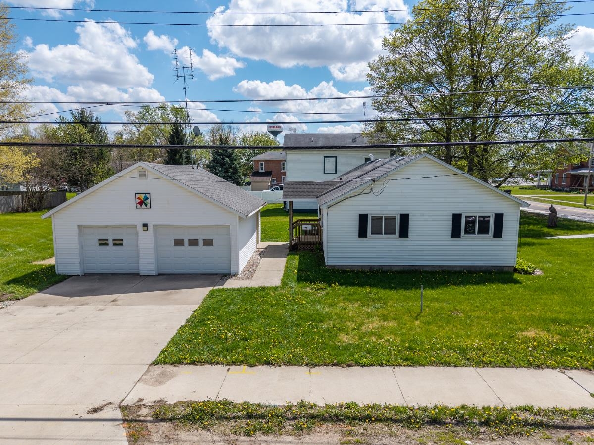 White siding residence featuring a two-car detached garage, a concrete driveway, and a well-maintained lawn
