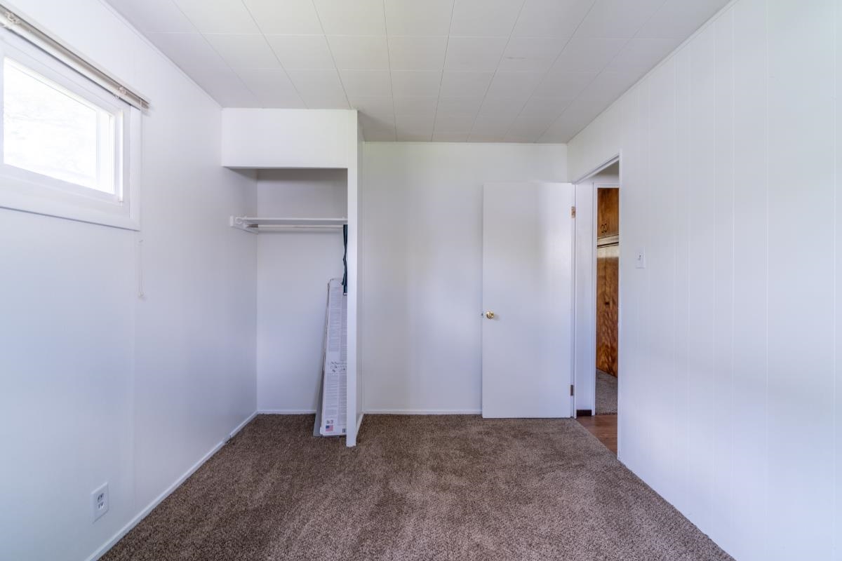 Bright interior room featuring a window, built-in closet with hanging rod, and neutral-toned carpet flooring