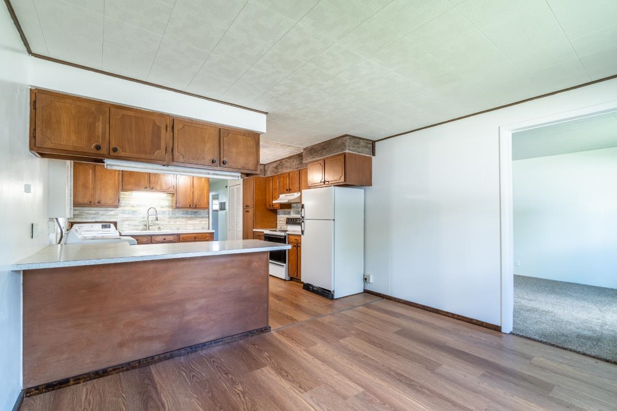 Kitchen featuring wood-finish flooring, wood cabinetry, a breakfast bar with a light-toned countertop, and a tiled backsplash