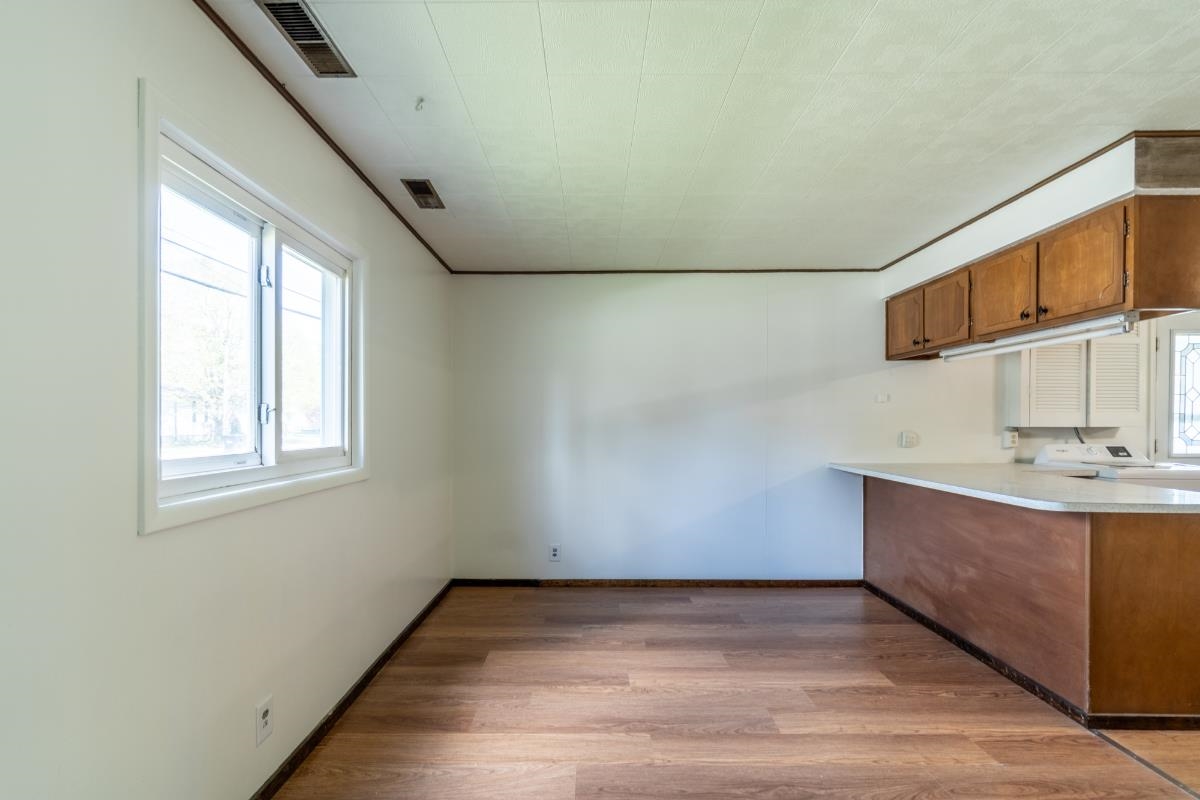 Open-concept living space with wood-finish flooring, a bright window, and a kitchen featuring wood cabinetry, a light-toned countertop, and built-in lighting