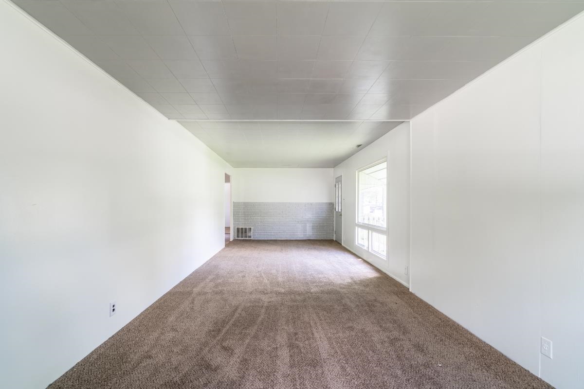 Spacious room featuring neutral carpet flooring, white painted walls, and a large window providing ample ambient light