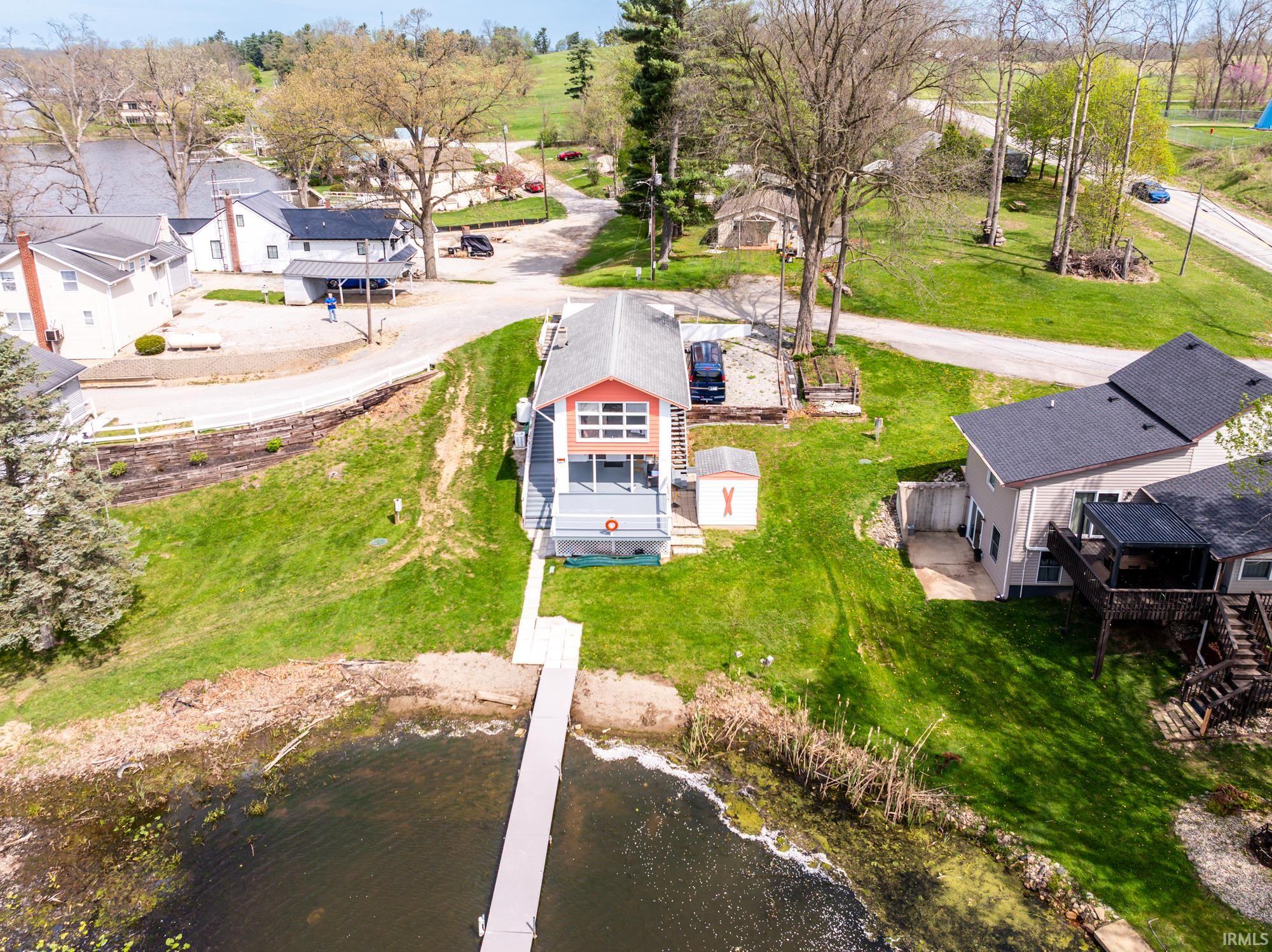 Waterfront property featuring a private dock, a two-story residence with a balcony, an adjacent storage shed, and a paved driveway