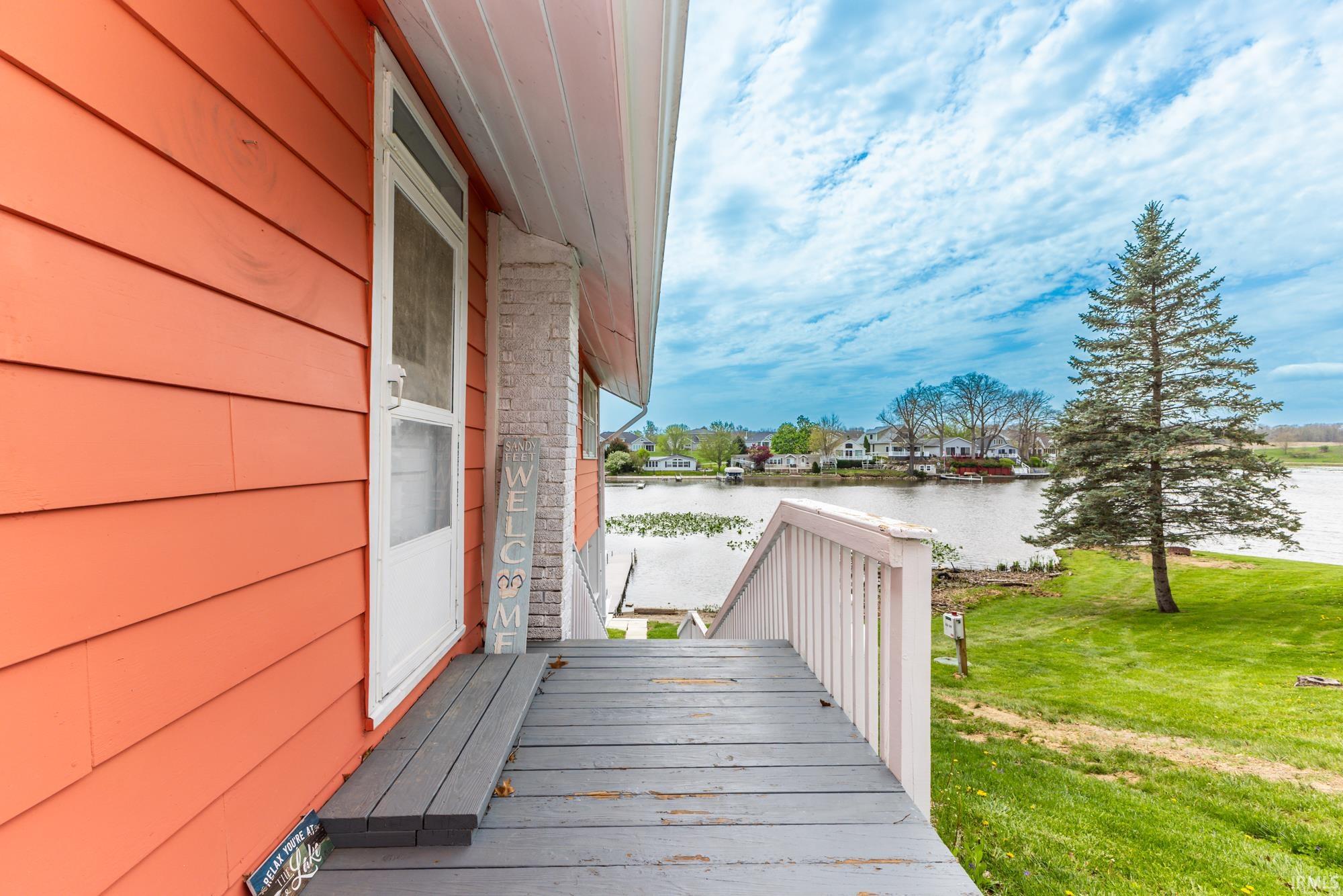 Waterside property featuring vibrant orange siding, a white screen door, and a grey porch leading to a grassy area