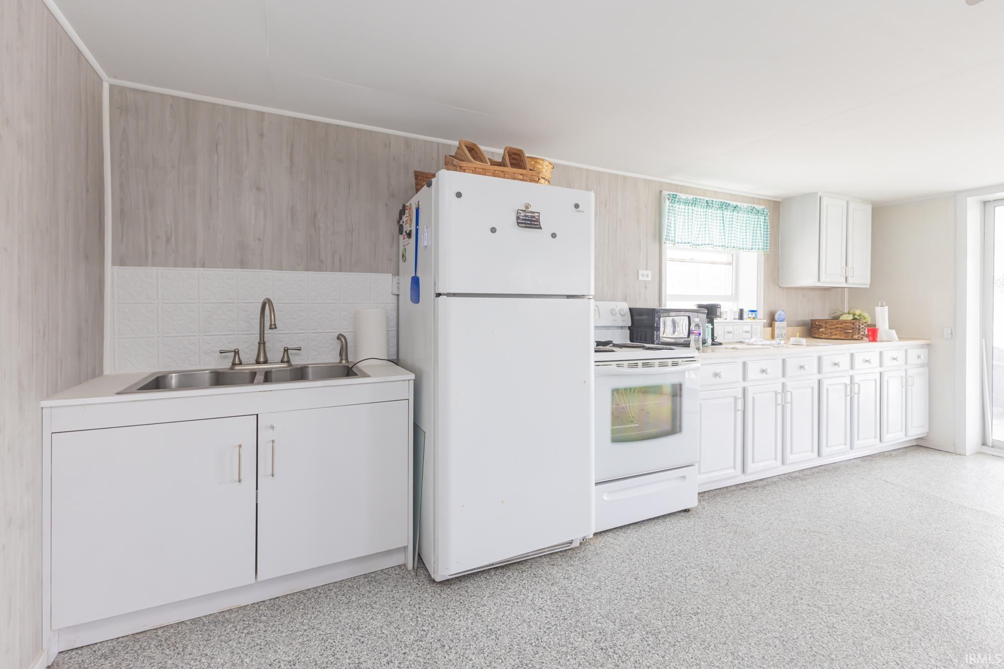 Kitchen featuring white cabinetry and appliances, wood-finish wall paneling, a double basin sink, and ample countertop space
