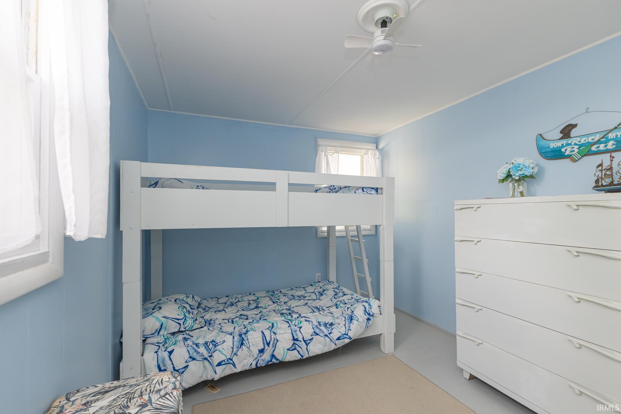 Bedroom featuring light blue walls, two windows, and a ceiling fan
