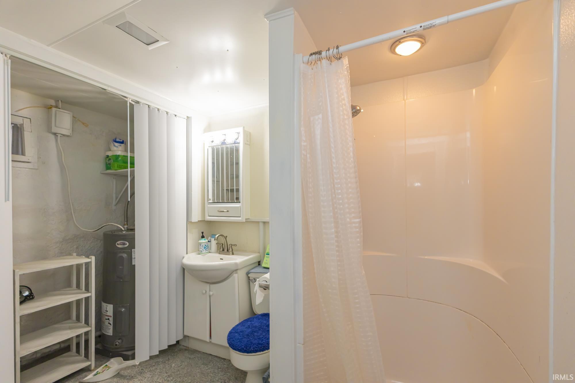 Compact bathroom featuring a stand-alone shower enclosure with an integrated light, a pedestal sink with a vanity cabinet, a toilet, and a medicine cabinet with integrated lighting