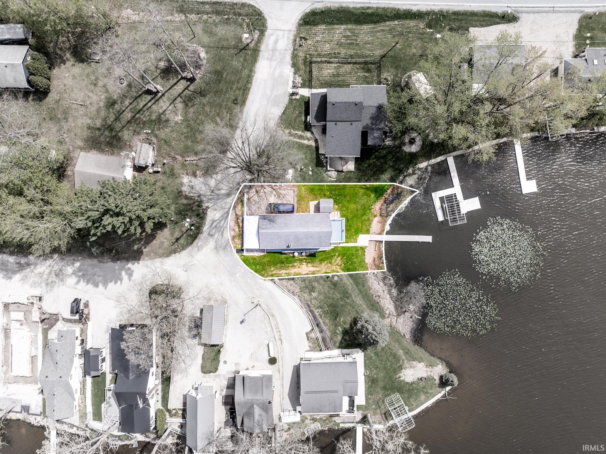 Waterfront property featuring a private dock, expansive green space, paved access road, and surrounding mature trees