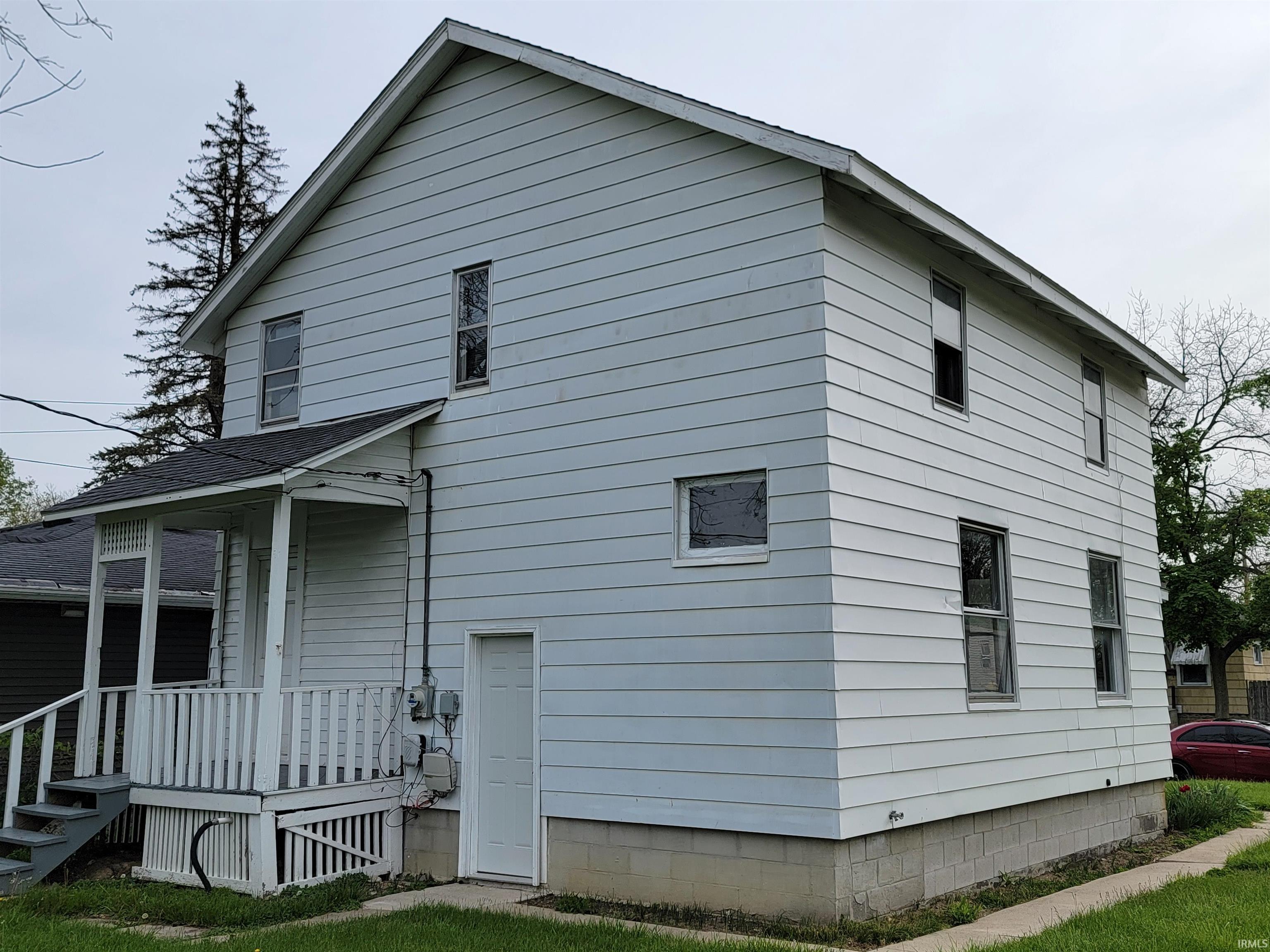 Two-story residential structure featuring white siding, a covered porch with white railings, exterior stairs, and a concrete block foundation