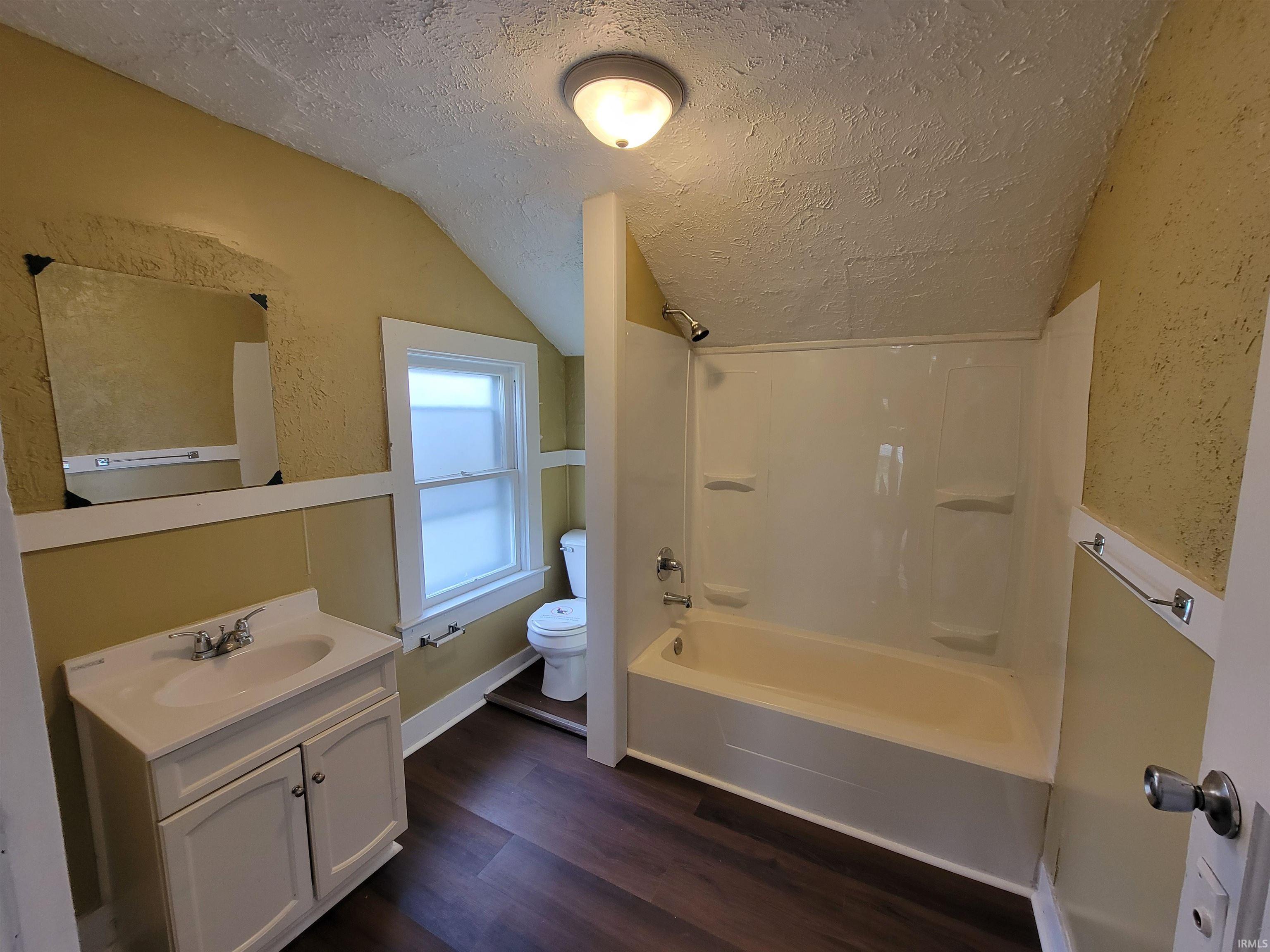 Bathroom featuring a white vanity with integrated sink, wood-finish flooring, a full bathtub with shower, and a privacy window
