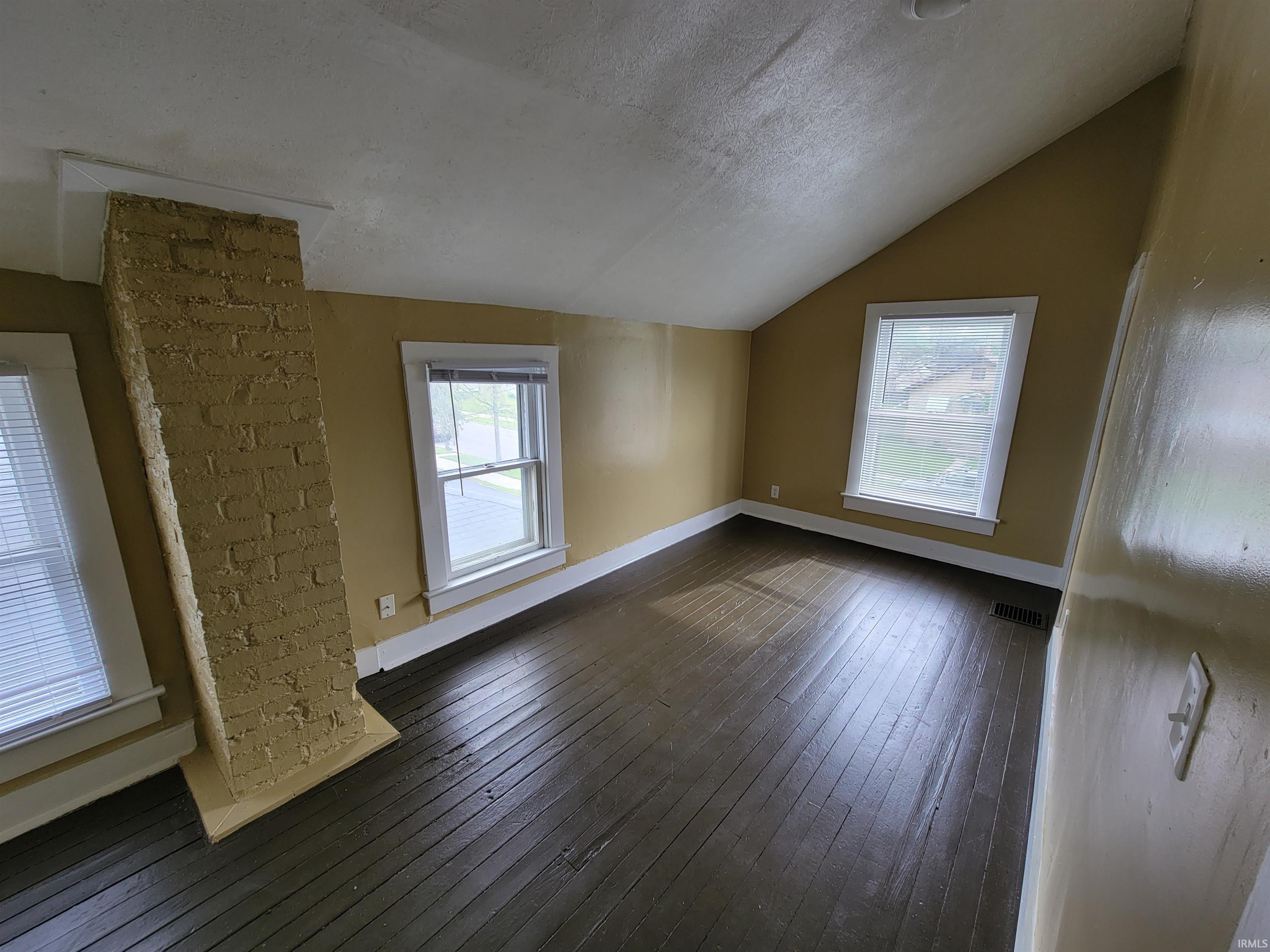 Attic space featuring dark wood-finish flooring, a painted brick column, and multiple windows with white trim