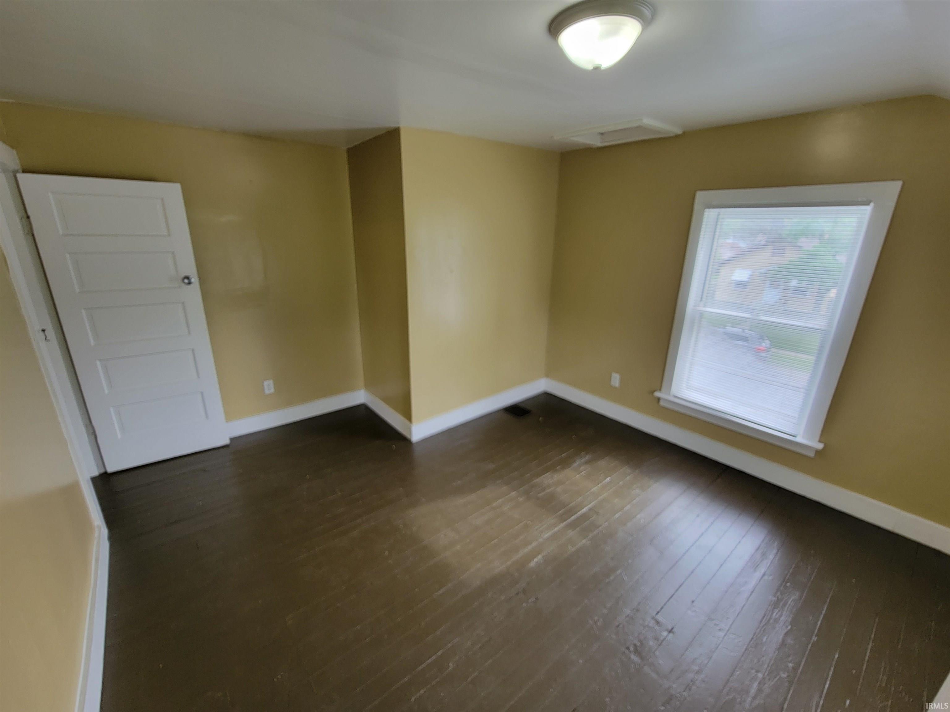 Room featuring wood-finish flooring, a window with white trim, a flush mount ceiling light, a built-in air vent, and a five-panel interior door