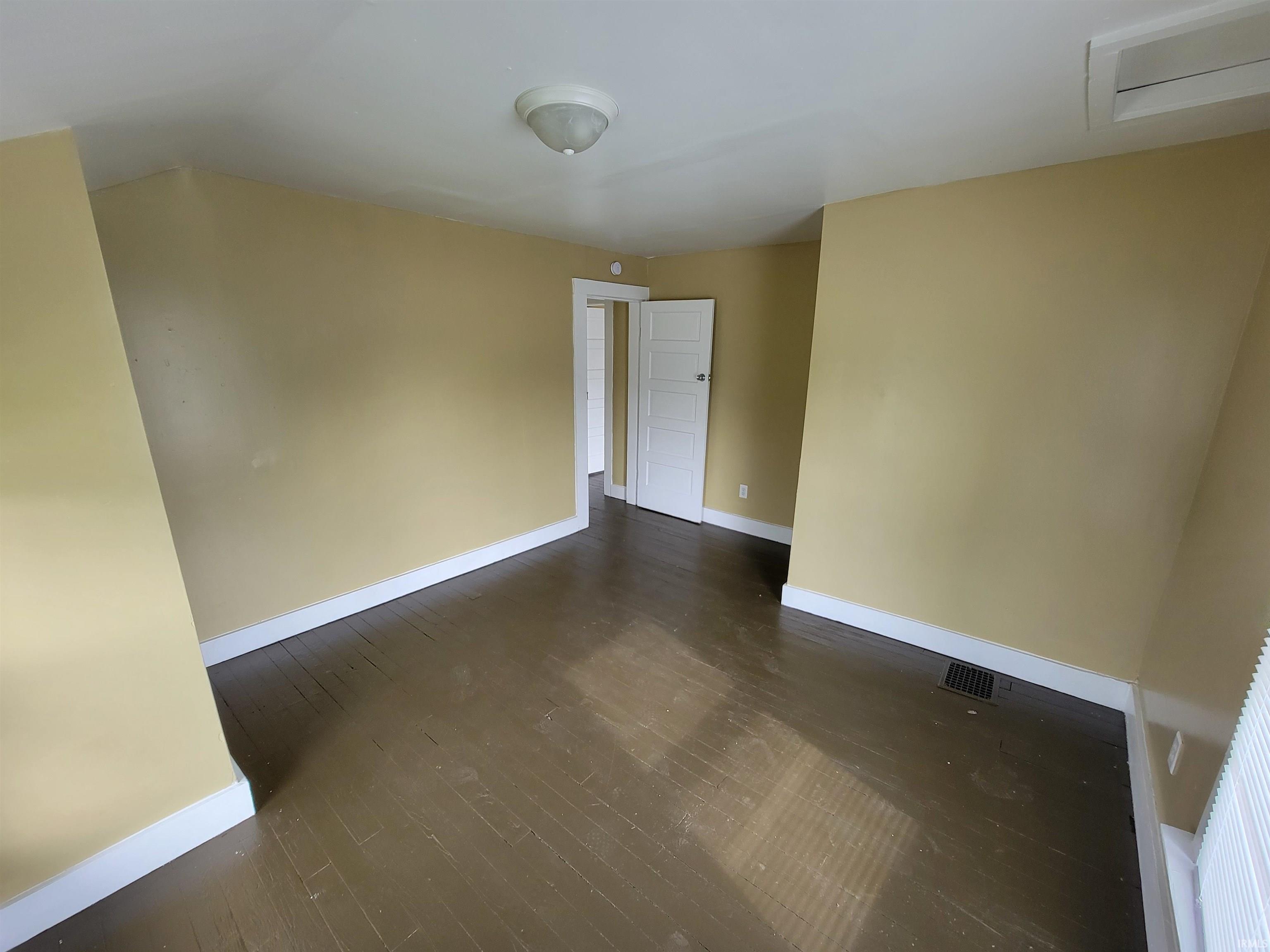 Room featuring dark wood-finish flooring, light yellow walls, and white trim