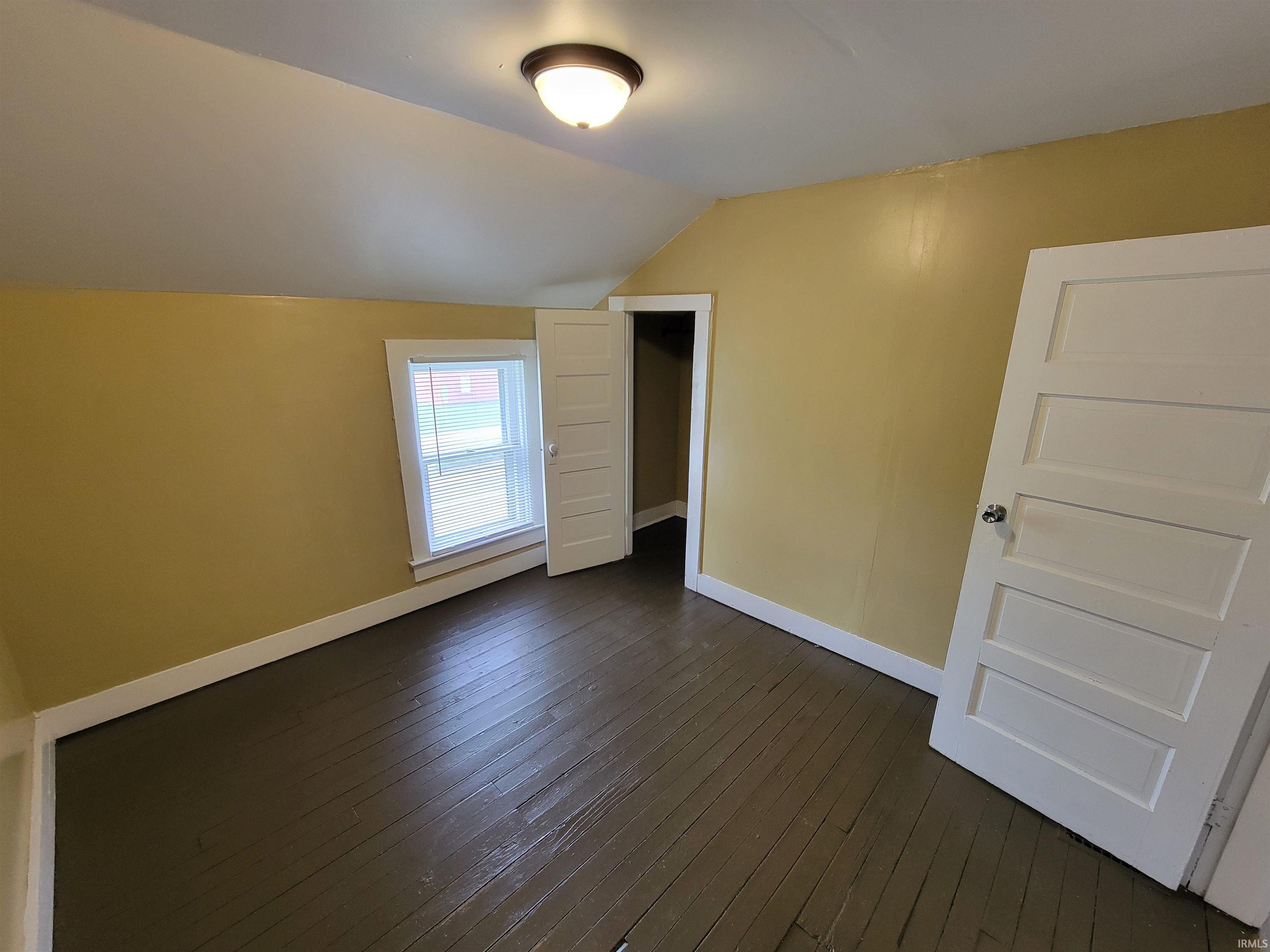 Room featuring wood-finish flooring, a window with blinds, and a paneled door
