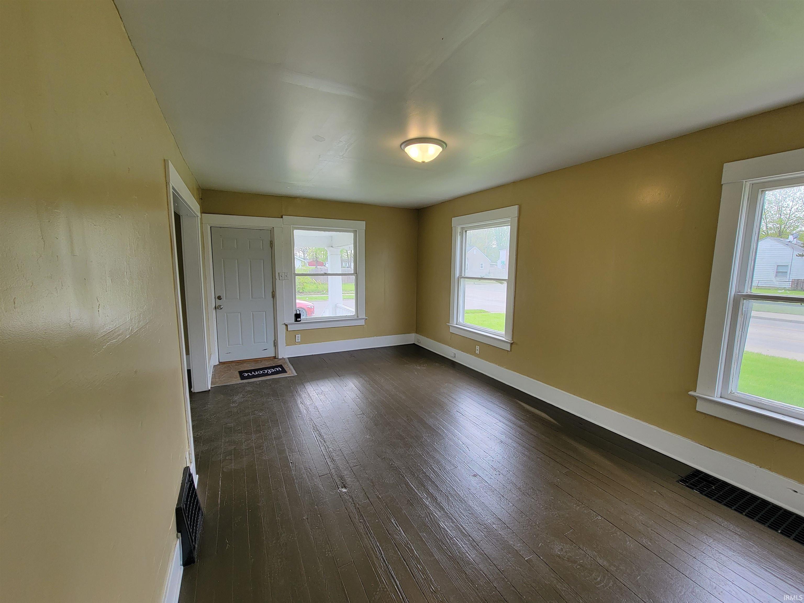 Spacious room featuring wood-finish flooring, multiple windows with white trim, and a ceiling-mounted light fixture