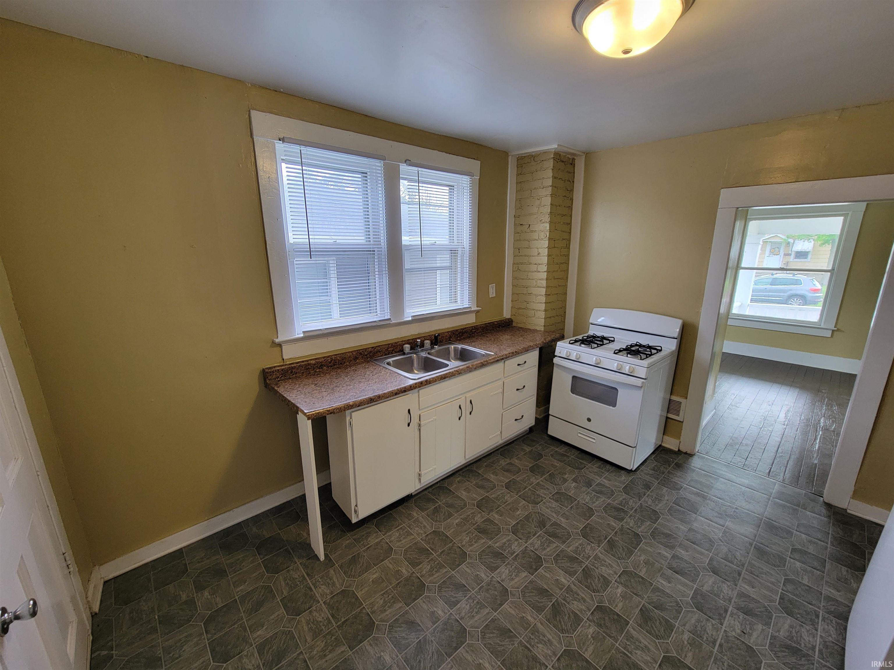 Kitchen featuring dual windows, white base cabinetry, integrated dual-basin stainless steel sink, a four-burner gas range, and patterned flooring