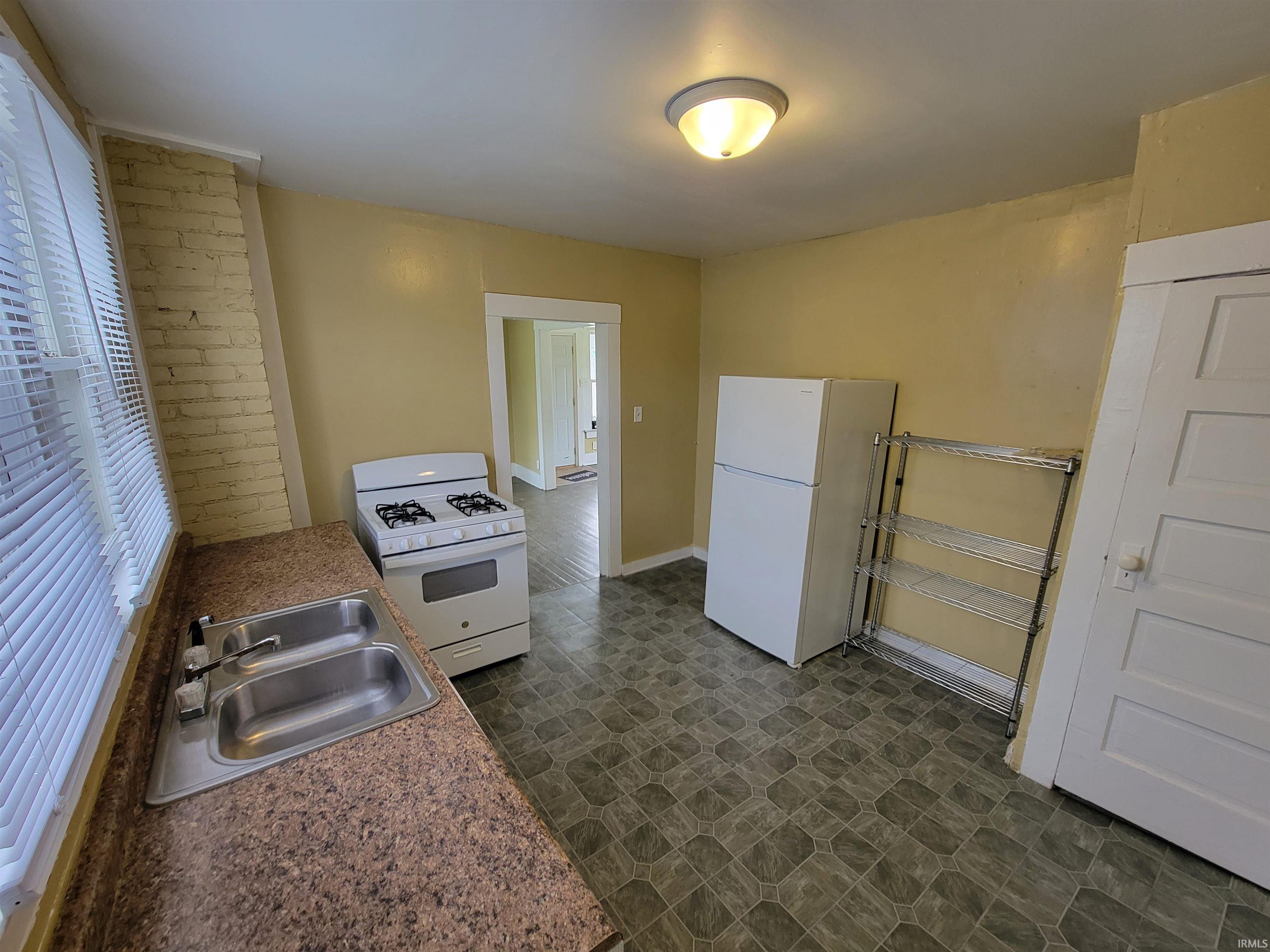 Kitchen featuring a double basin stainless steel sink, laminate countertops, vinyl flooring, and a window with blinds