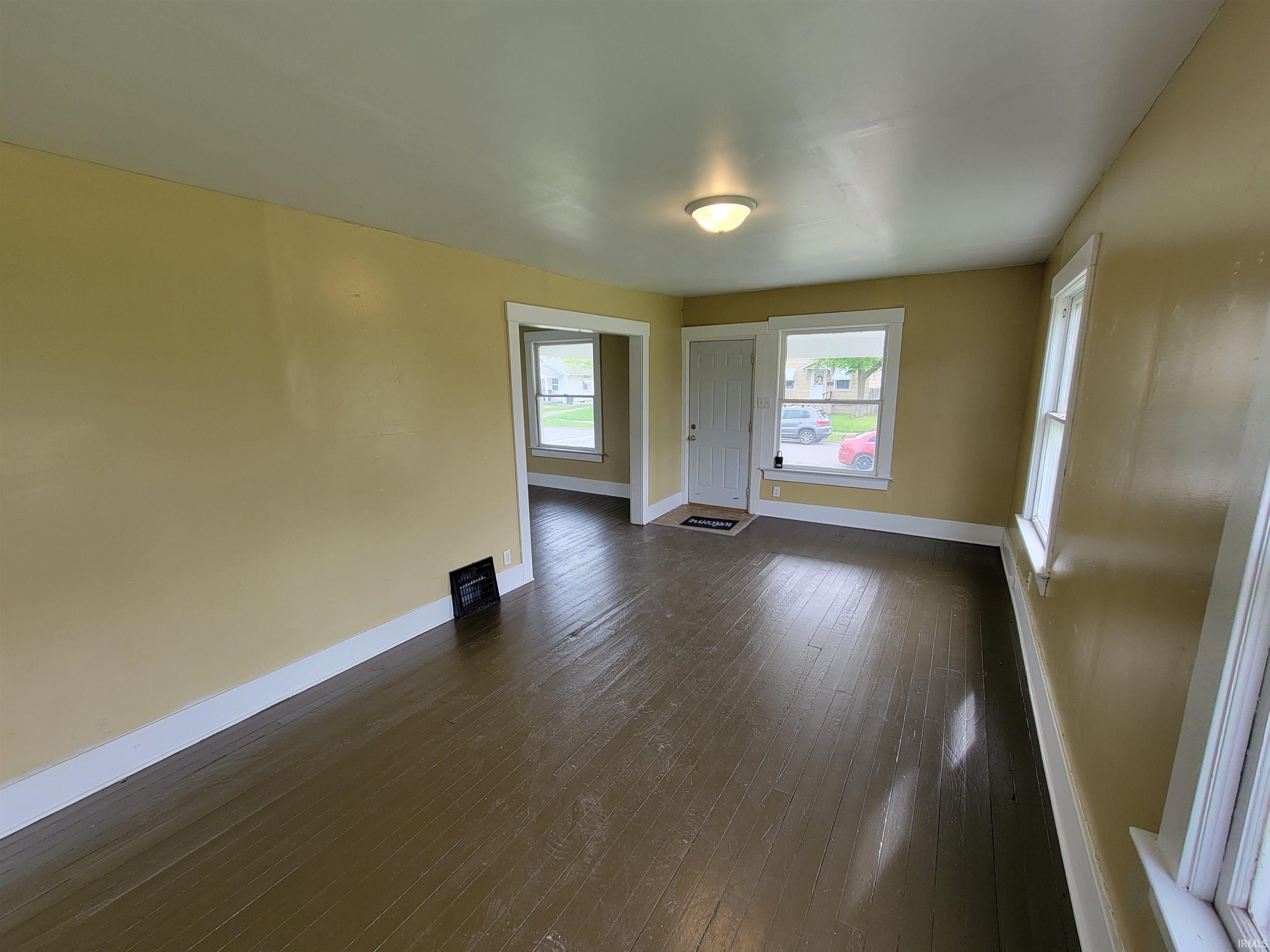 Spacious interior room featuring wood-finish flooring, light-toned walls, and multiple windows