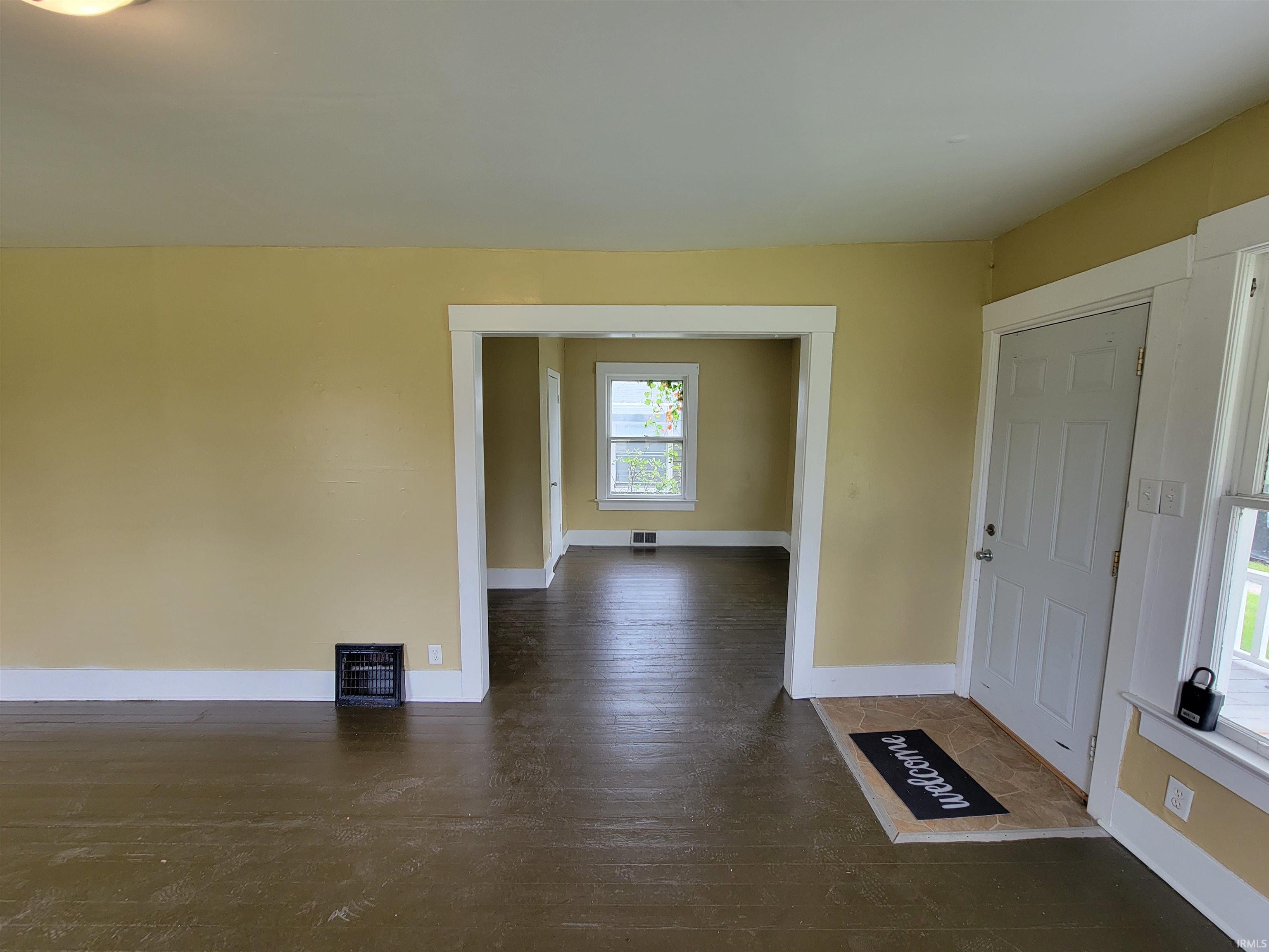 Spacious interior featuring a neutral wall color, dark wood-finish flooring, white trim, and a white paneled door