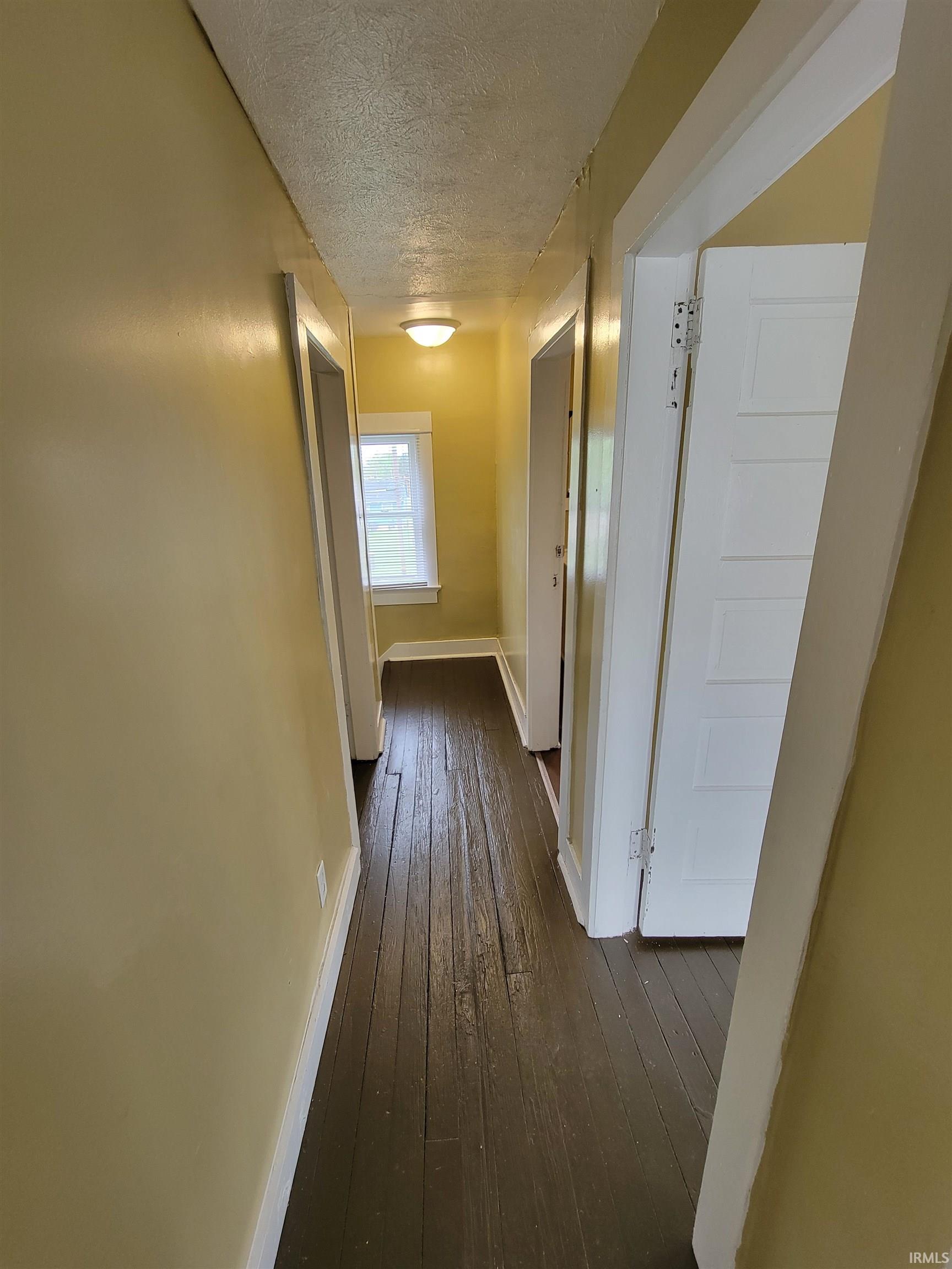 Hallway with dark wood-finish flooring, light yellow painted walls, and white trim