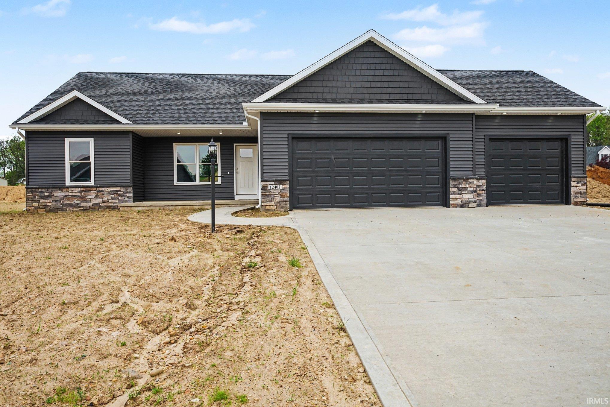Contemporary exterior featuring dark gray siding, complementary stone accents, a multi-car garage, and a concrete driveway