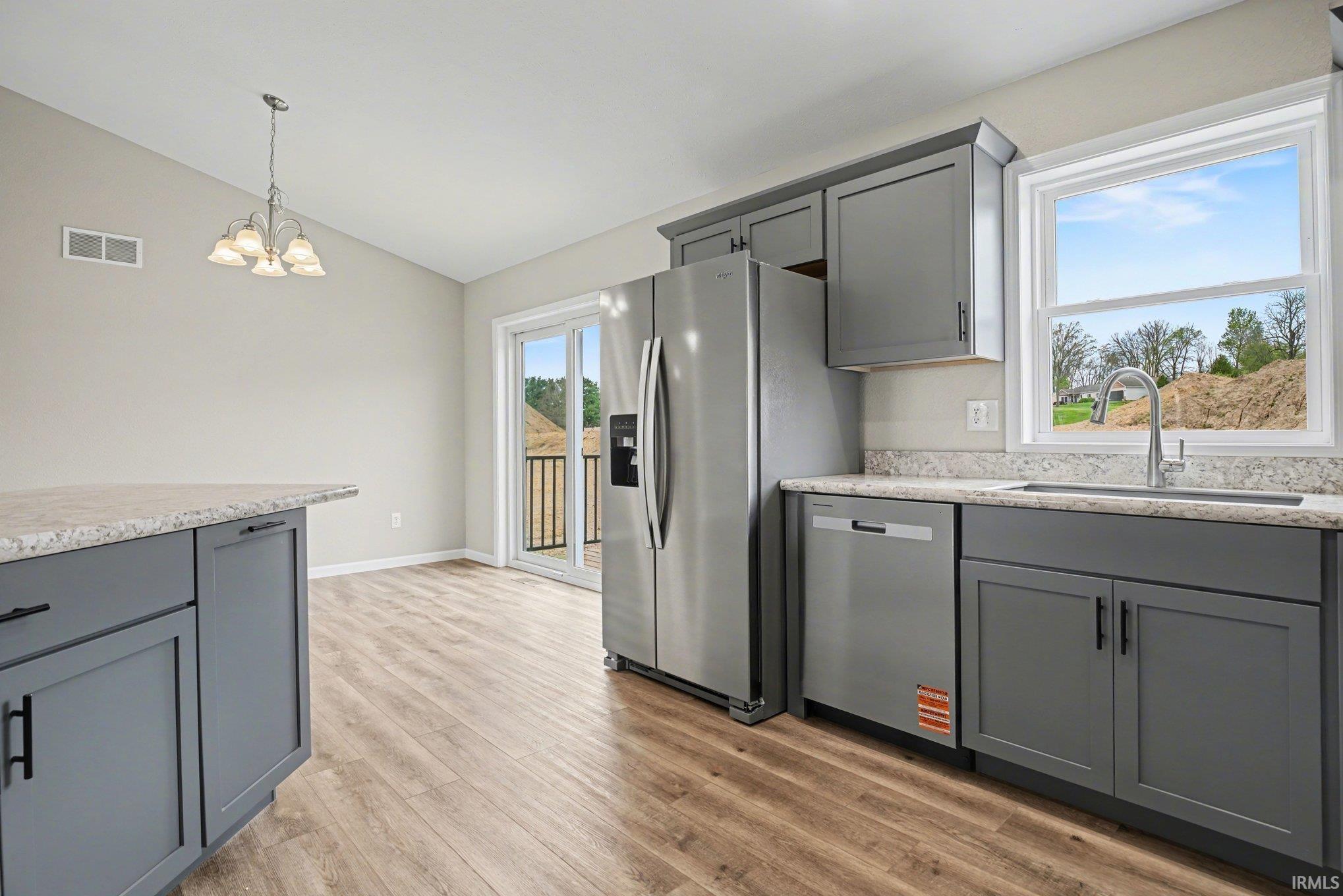 Kitchen featuring dark gray cabinetry with black hardware, wood-finish flooring, light-toned countertops, and stainless steel appliances