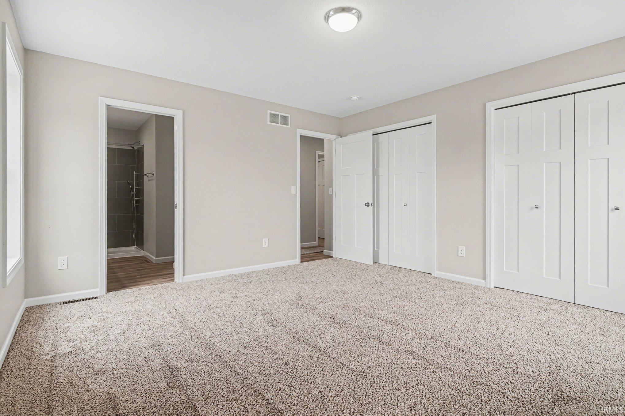 Spacious room with plush carpet flooring, light neutral wall tones, two paneled bi-fold closet doors, a recessed ceiling light fixture, and an open doorway leading to a bathroom with a shower
