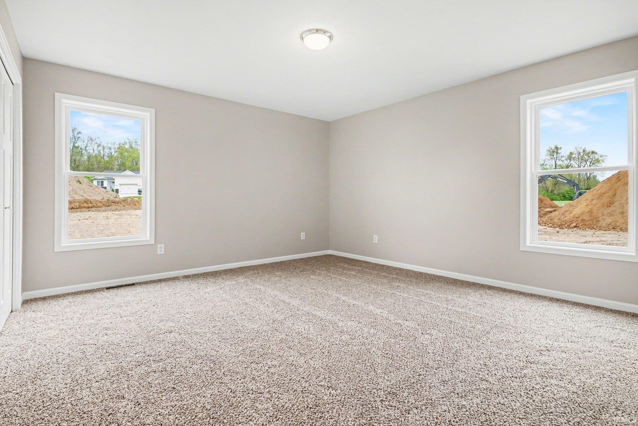 Spacious room featuring neutral paint, plush carpet flooring, a flush-mount ceiling light, and two large windows with white trim