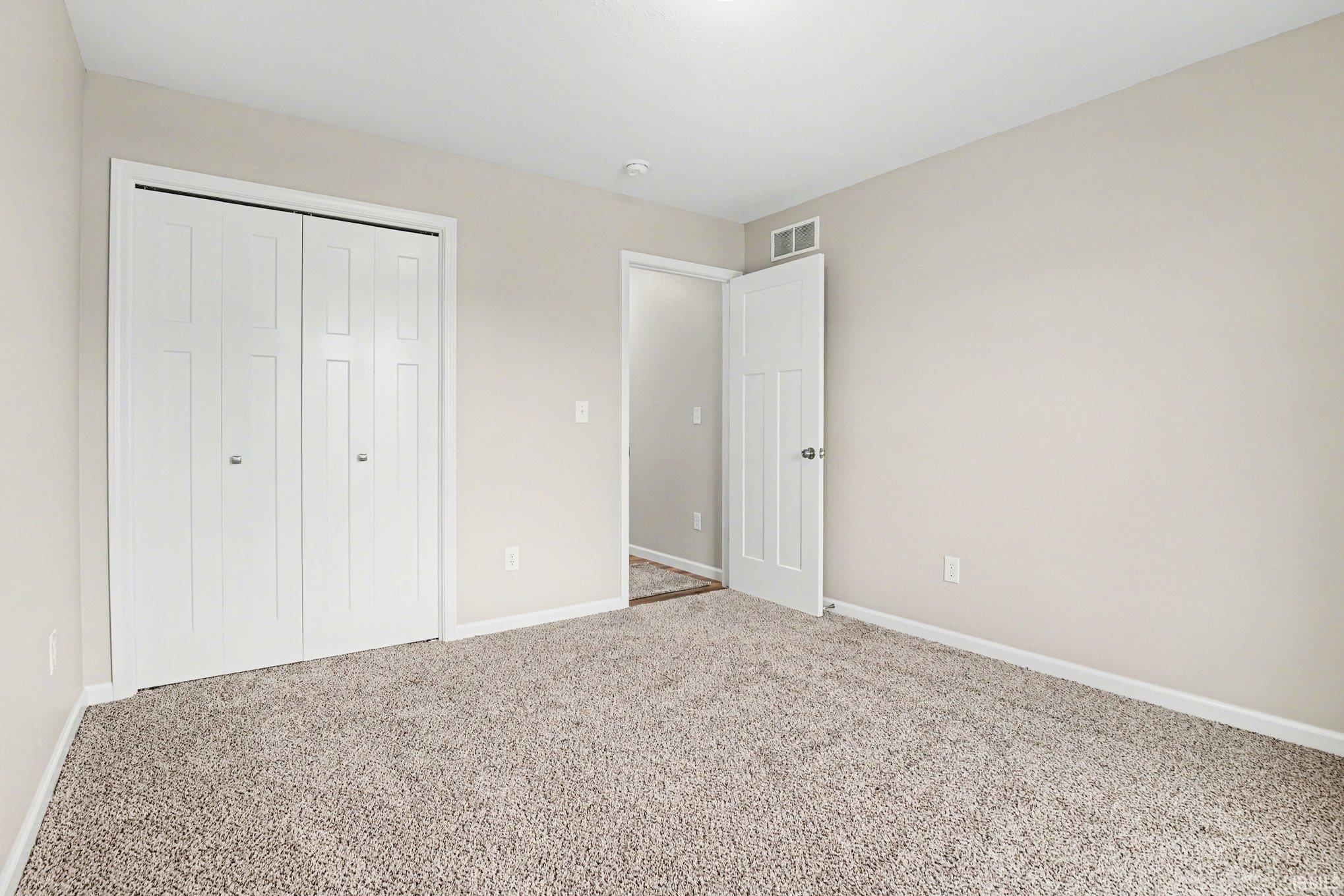 Spacious room featuring neutral carpeting, light-toned wall paint, white trim, and a bi-fold closet with panel doors