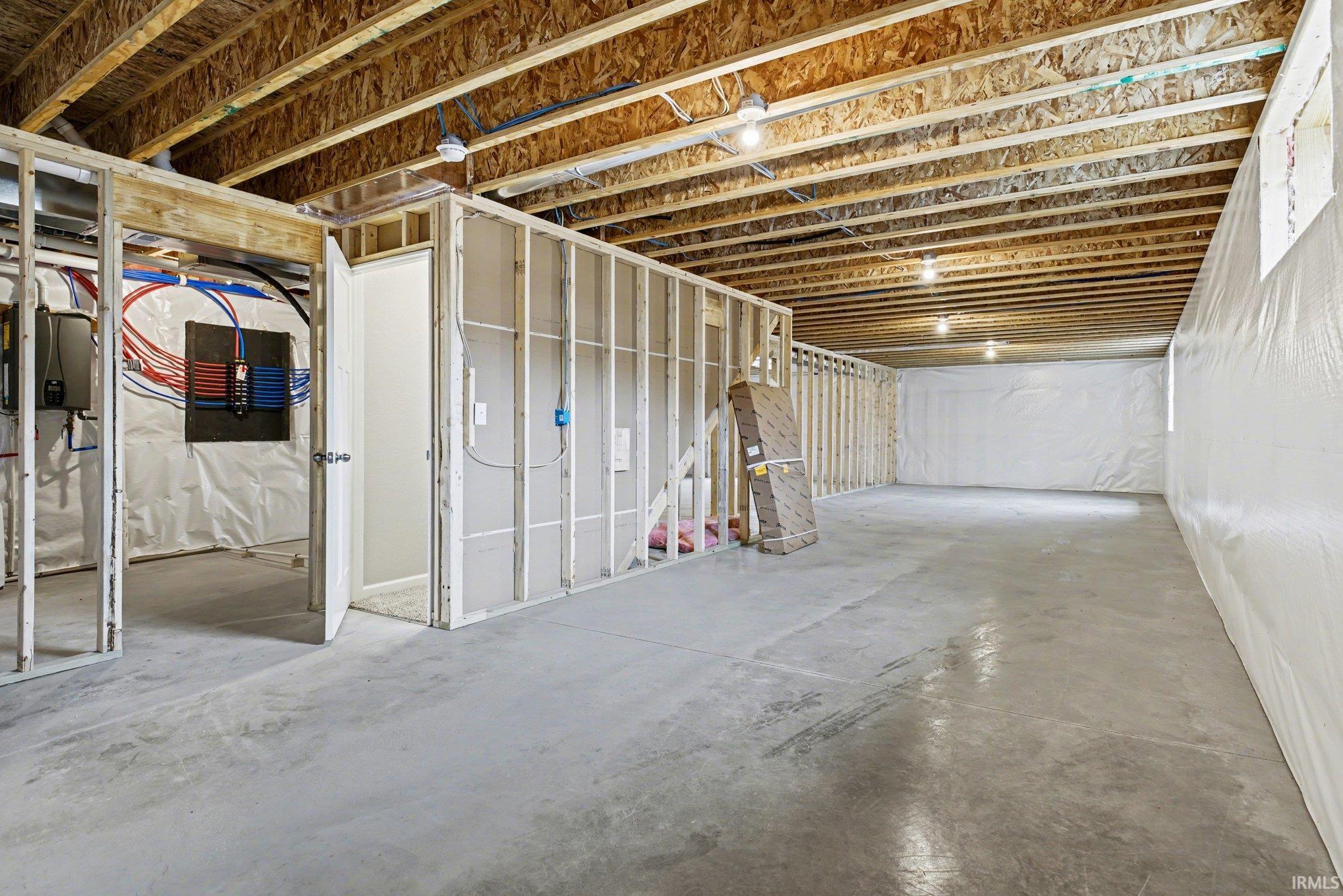 Unfinished basement space featuring exposed wood joists, concrete flooring, framed interior walls, and perimeter wall insulation