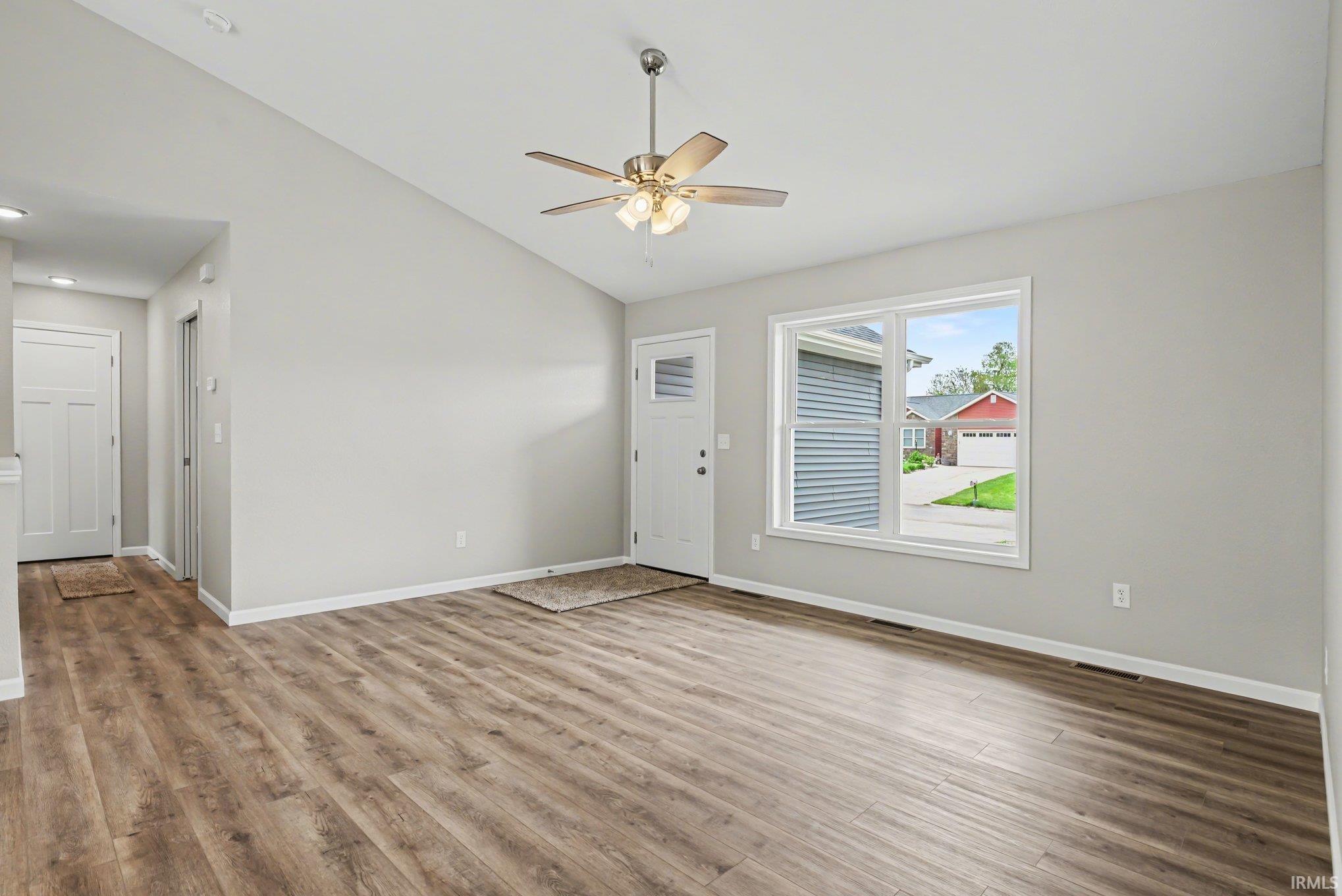 Spacious living area featuring a vaulted ceiling with a ceiling fan, wood-finish flooring, and a large window