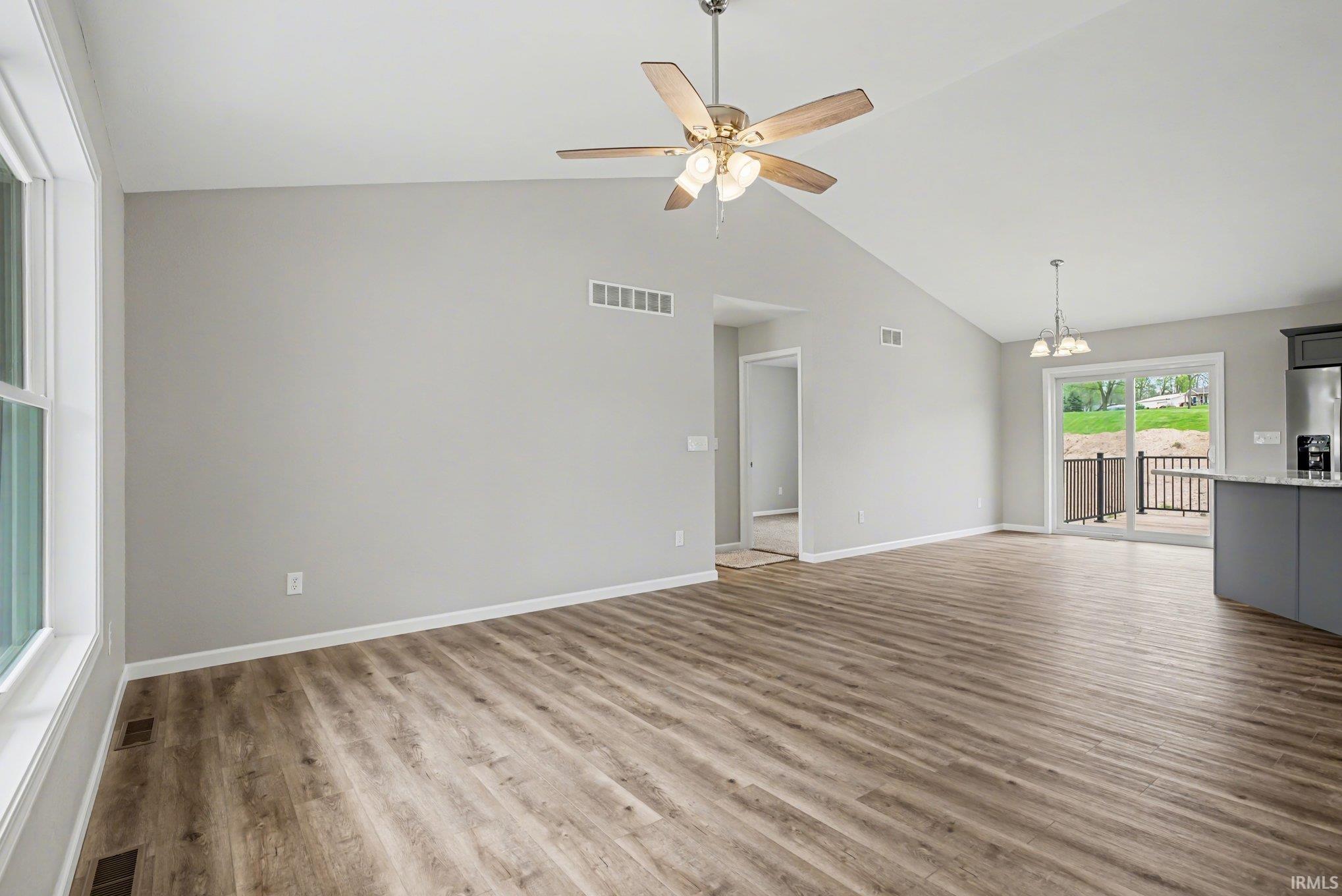 Expansive living area featuring vaulted ceilings, wood-finish flooring, a ceiling fan with integrated lighting, and a sliding glass door leading to an outdoor deck
