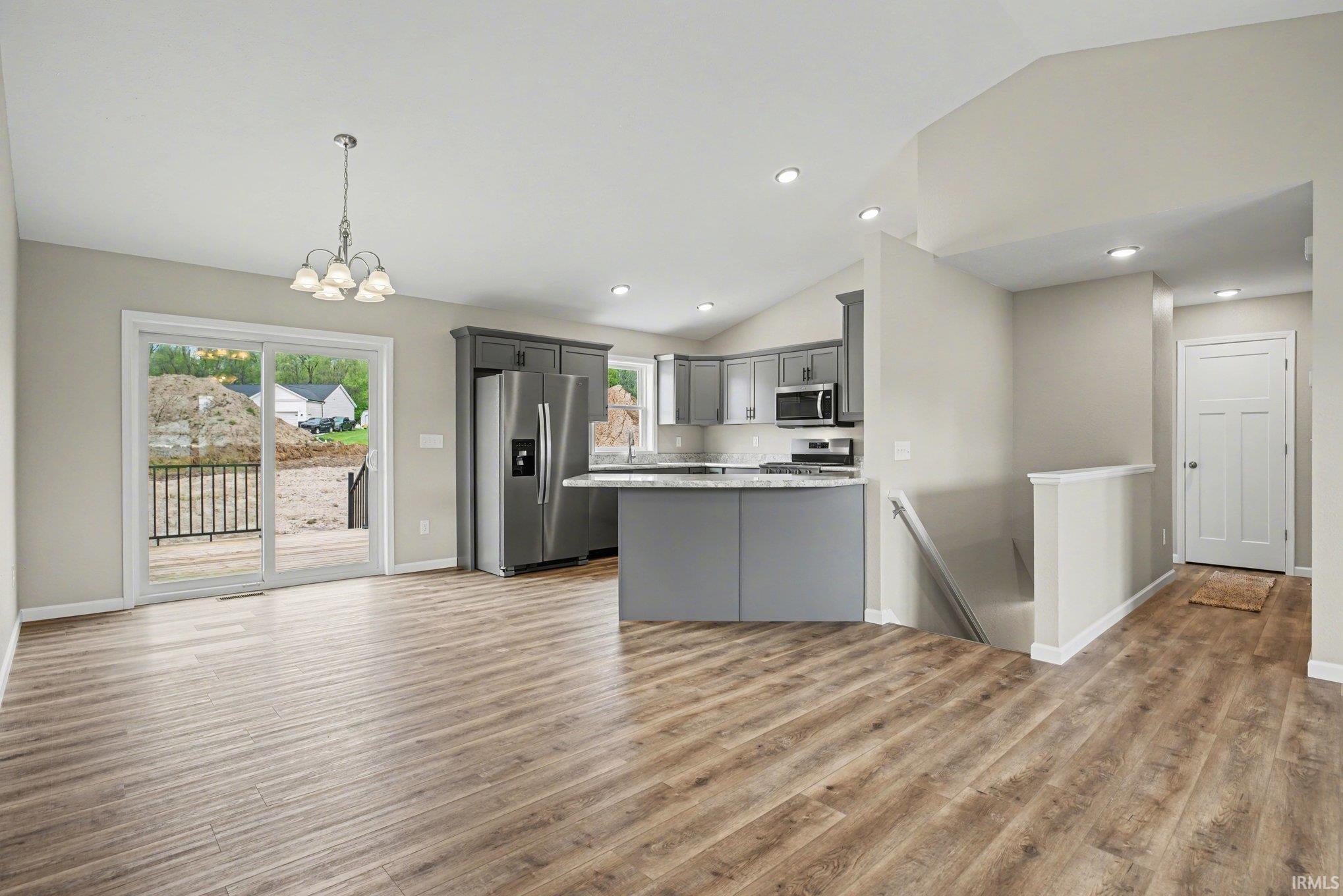 Open-concept living area featuring wood-finish flooring, a kitchen with grey cabinetry and stainless steel appliances, a breakfast bar, recessed lighting, and a sliding glass door opening to an outdoor deck