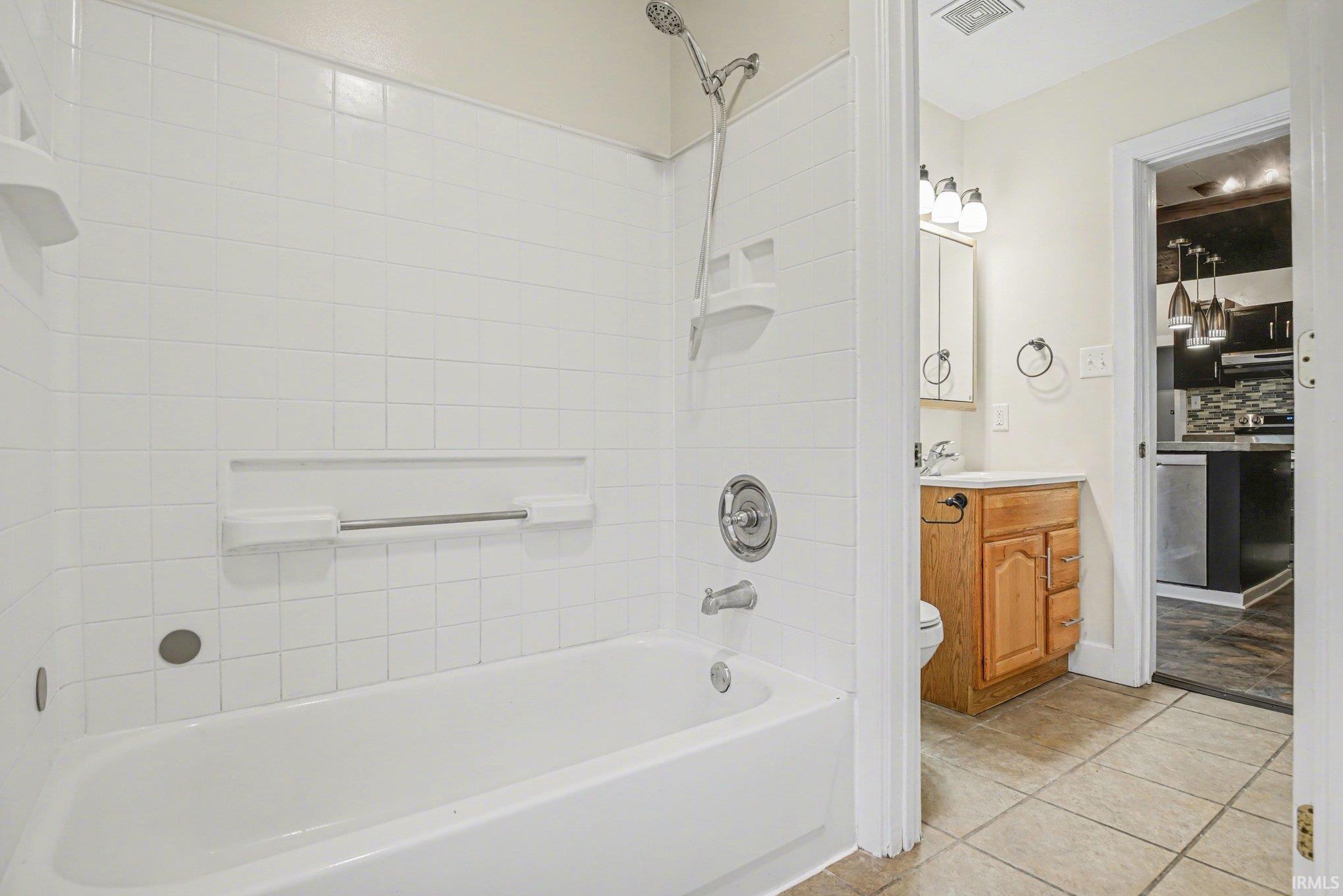 Bathtub and shower combination featuring white square-tiled surround, built-in shelving, and a chrome shower fixture