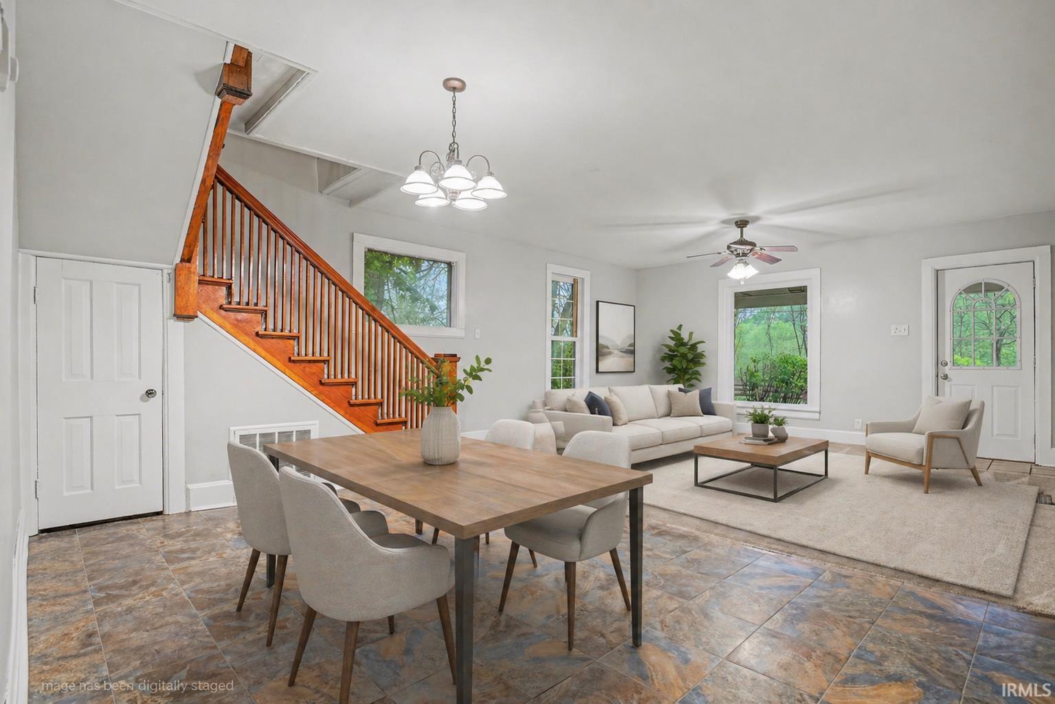 Open-concept living space featuring wood staircase, neutral wall tones, multi-tone tile flooring, and ample natural light