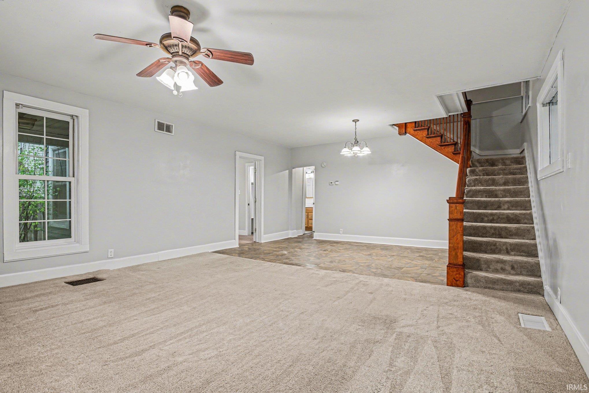 Spacious room featuring neutral carpeting, light gray walls, a ceiling fan with light fixture, and a window with white trim