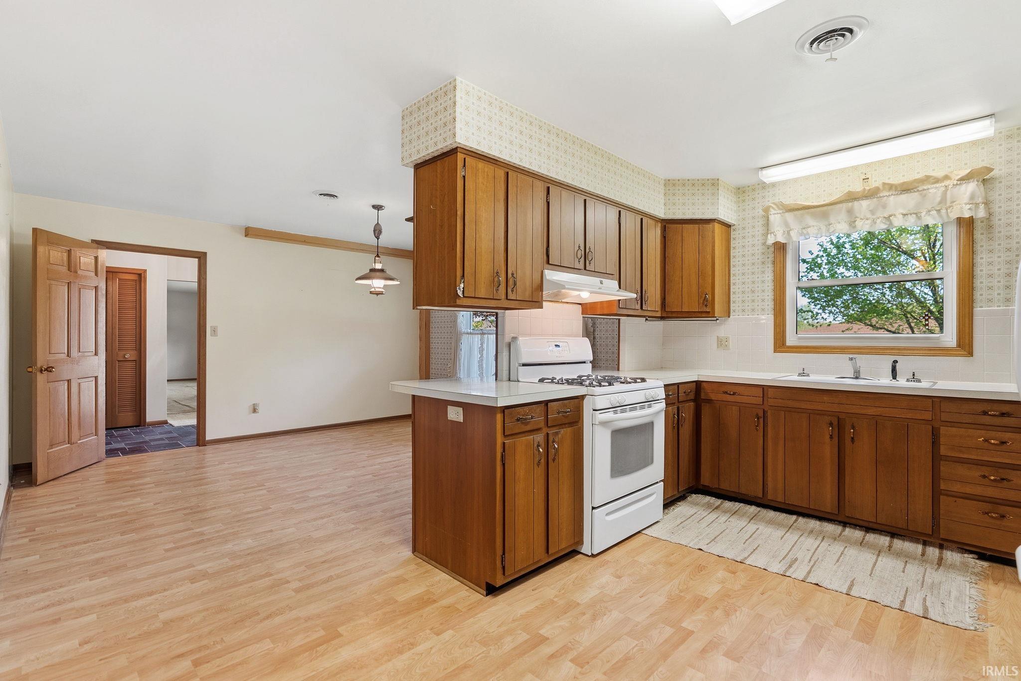 Kitchen featuring wood-finish cabinetry, white countertops, and a white gas range with overhead hood
