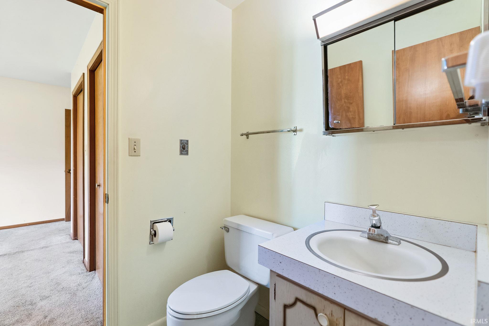 Bathroom featuring an integrated vanity sink with a laminate countertop, a mirrored medicine cabinet, a toilet, and light-colored walls