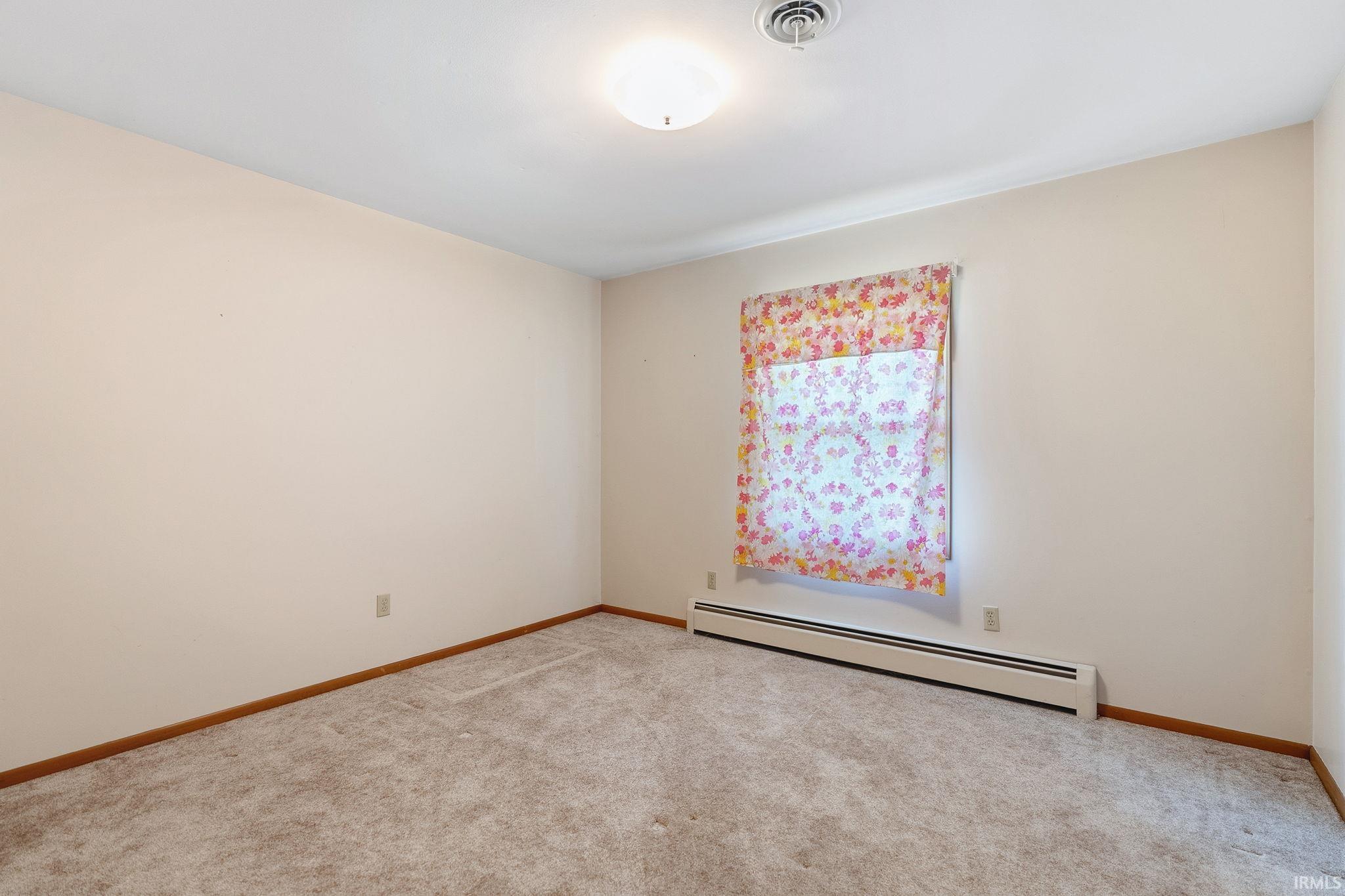 Room featuring neutral wall tones, light-toned carpet flooring, and a baseboard heating unit