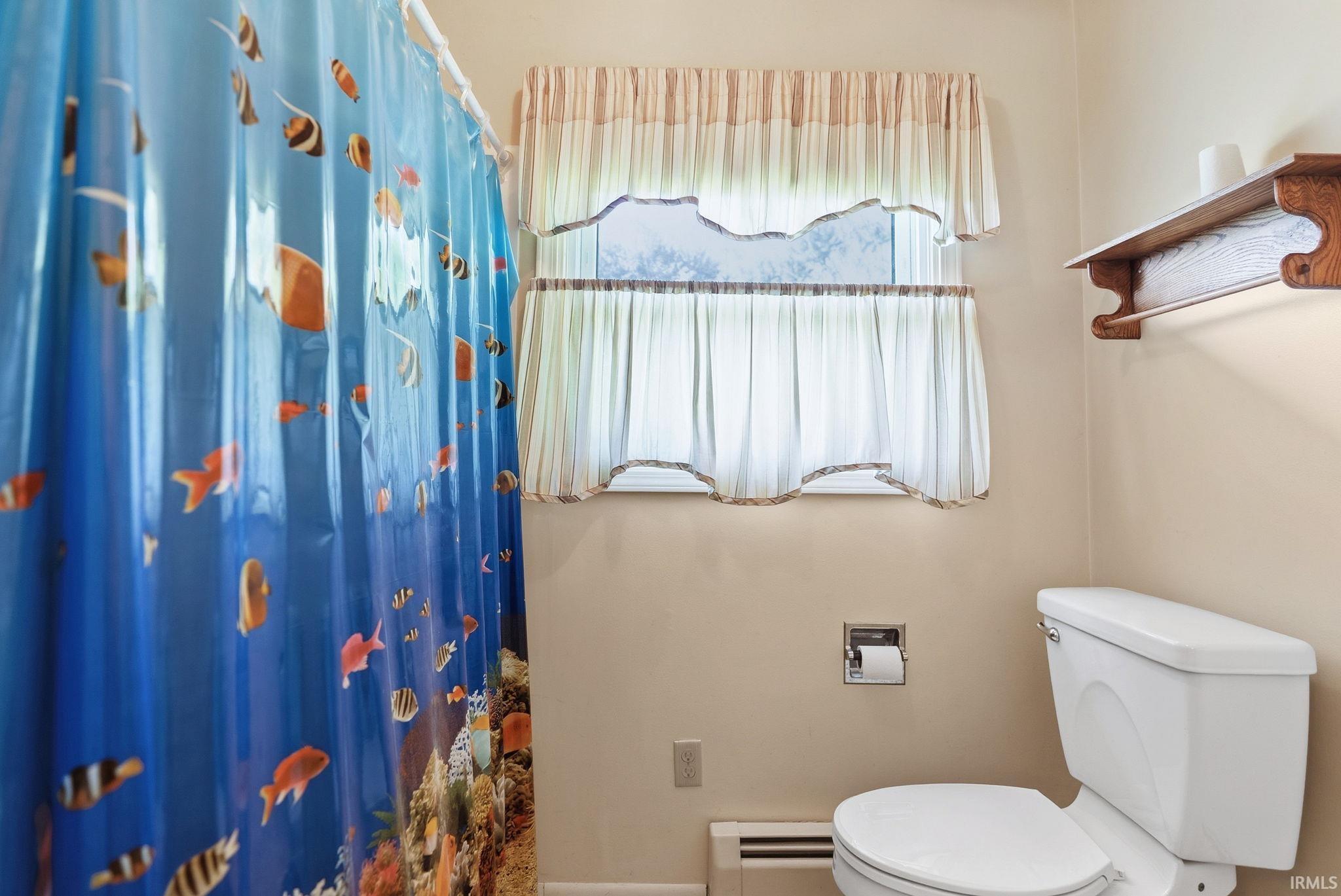 Bathroom featuring a standard toilet, window with privacy curtains, and wall-mounted shelving