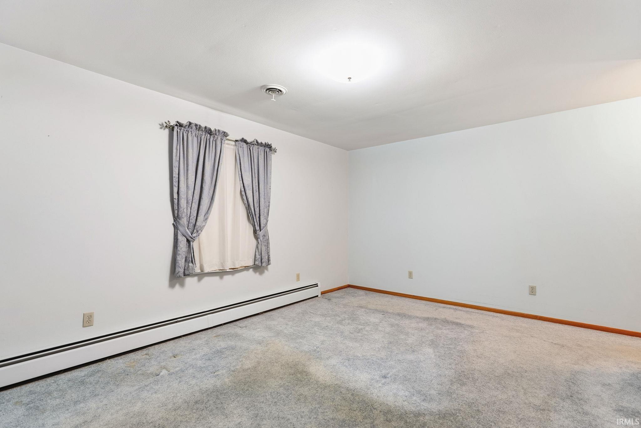 Interior room featuring a single window, light gray carpet, white walls, and wood-finish baseboards
