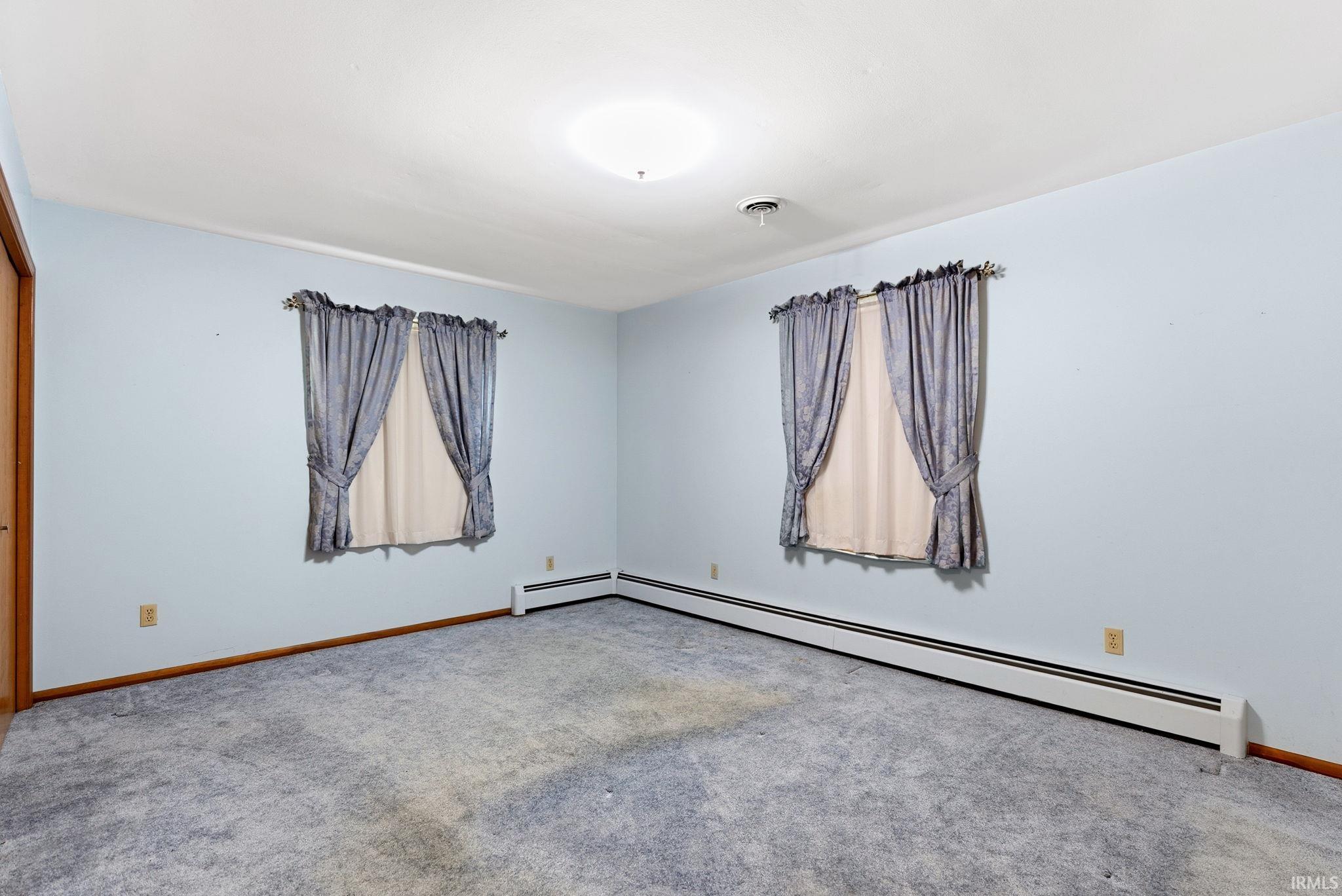 Spacious room featuring light blue walls, gray carpet, and two windows with tie-back drapery
