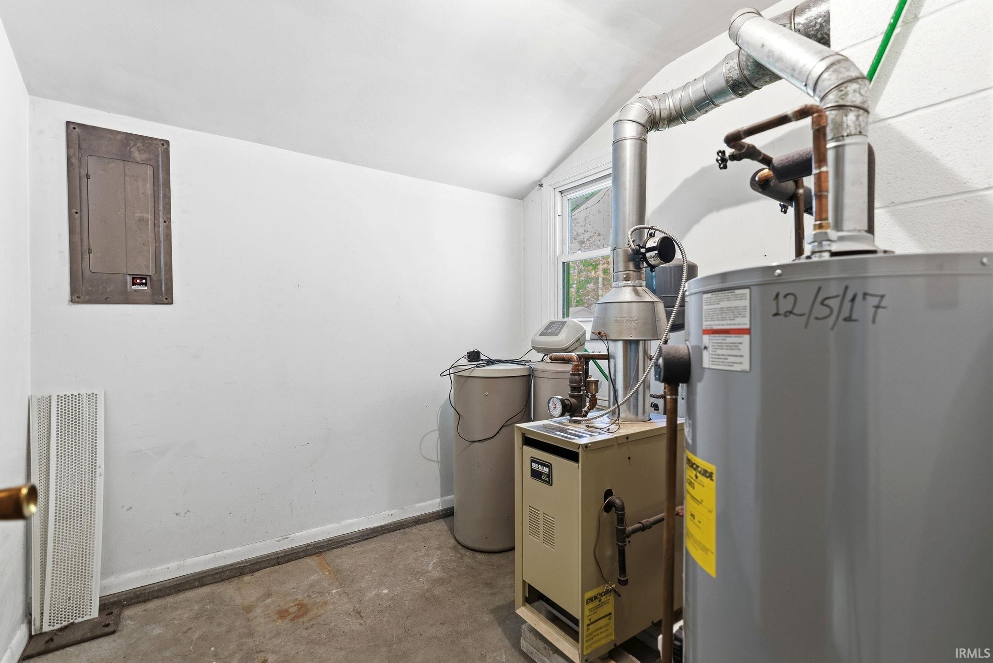 Utility room featuring exposed mechanical systems, a water heater, furnace, electrical panel, and a small window