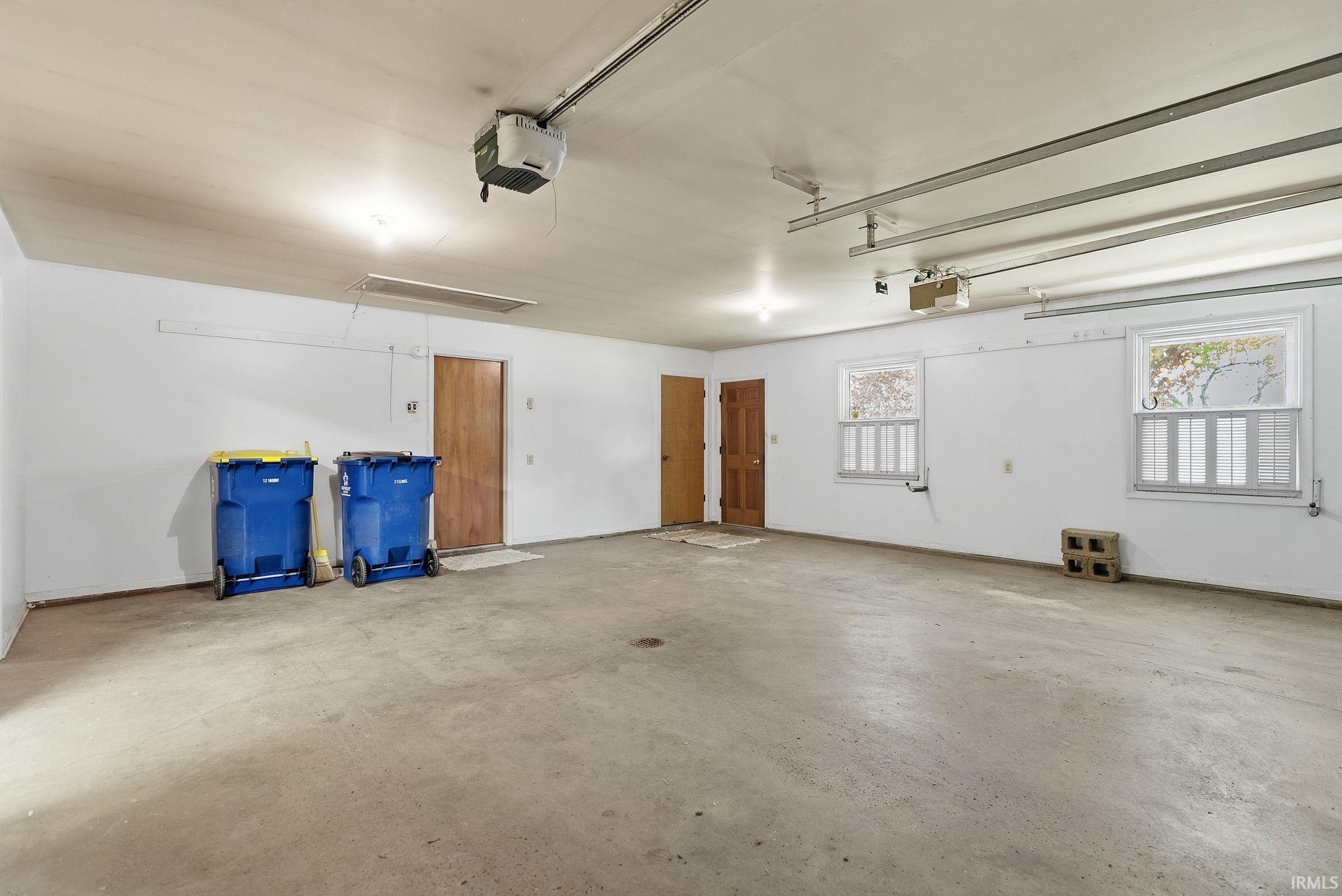 Spacious garage featuring concrete flooring, multiple windows, two wooden entry doors, and overhead lighting